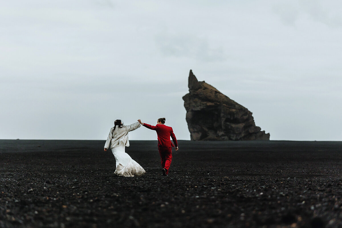 married couple is happily running towards a cliff on the south coast of Iceland