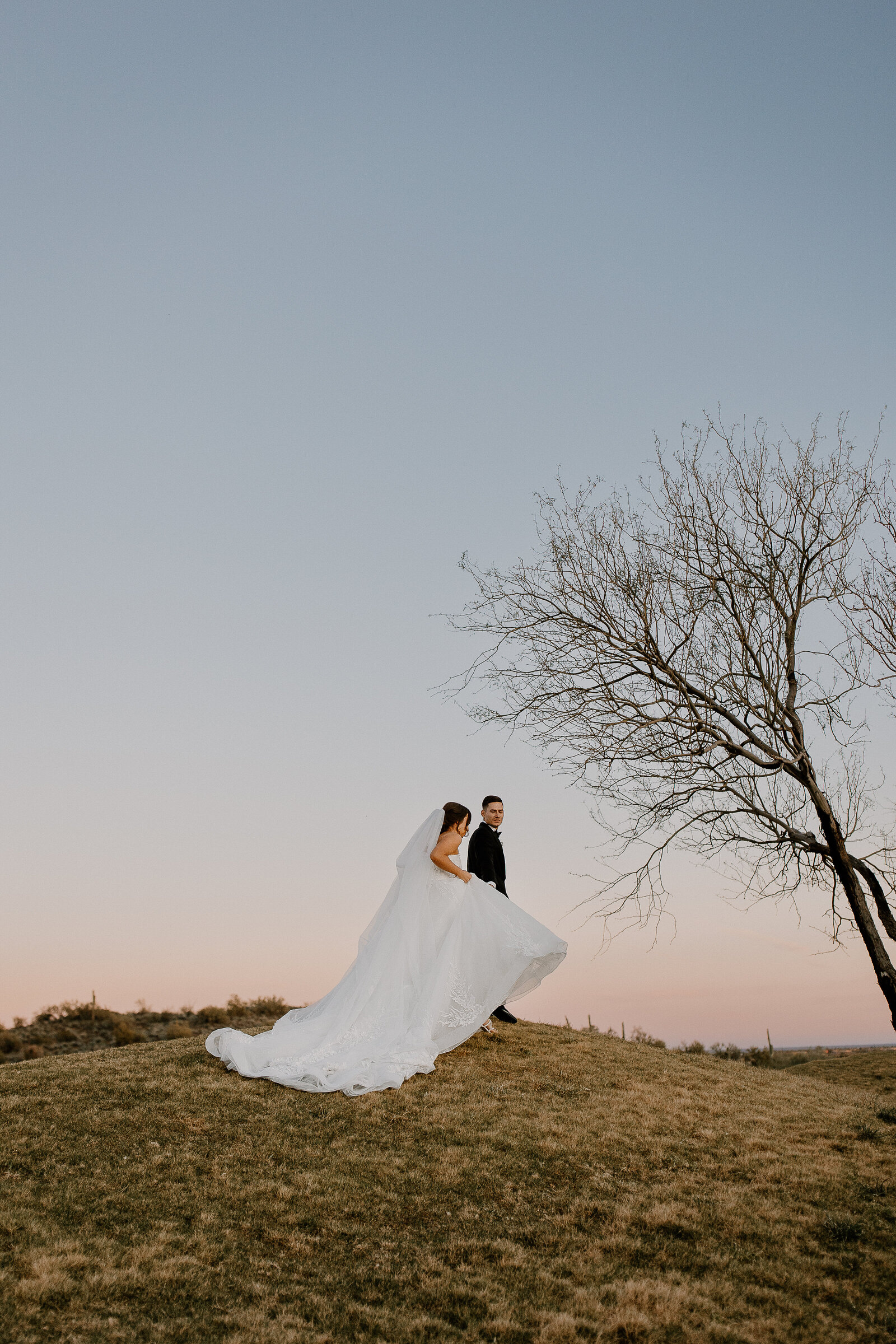 A bride and groom walking along a hill at sunset.