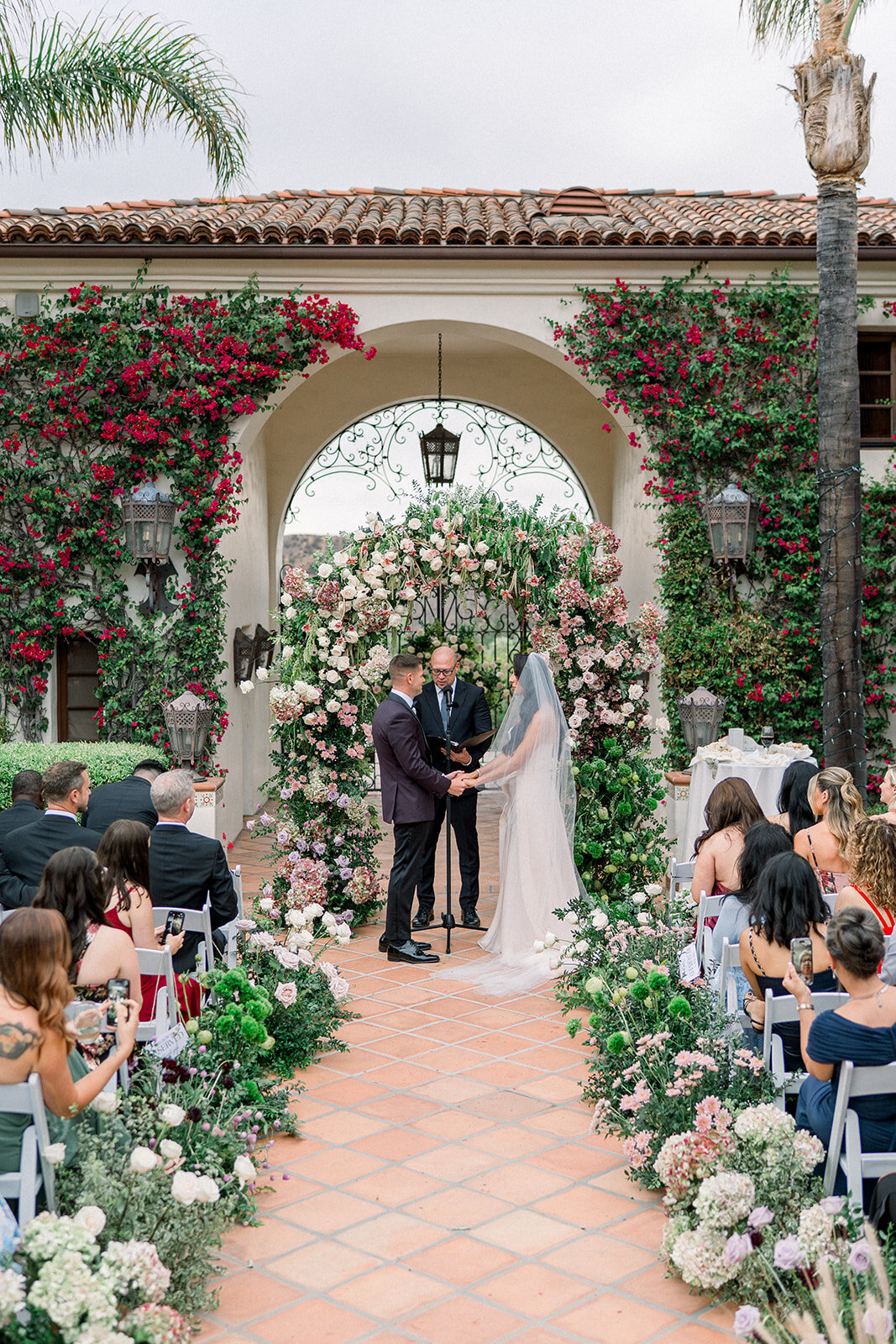 Guests look on as the couple exchanges vows beneath a floral ceremony arch at the iconic Hummingbird Nest Ranch.