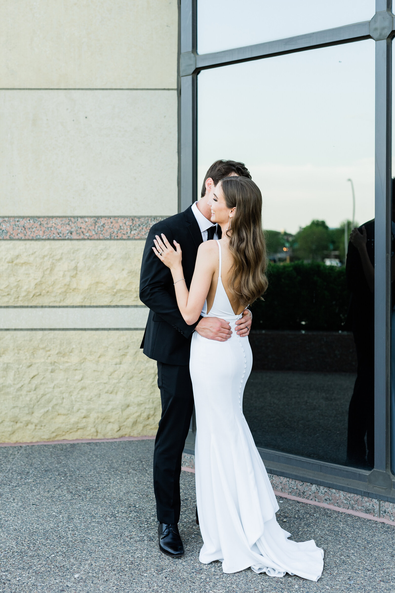 Wedding couple sharing kiss in front of a large corner window