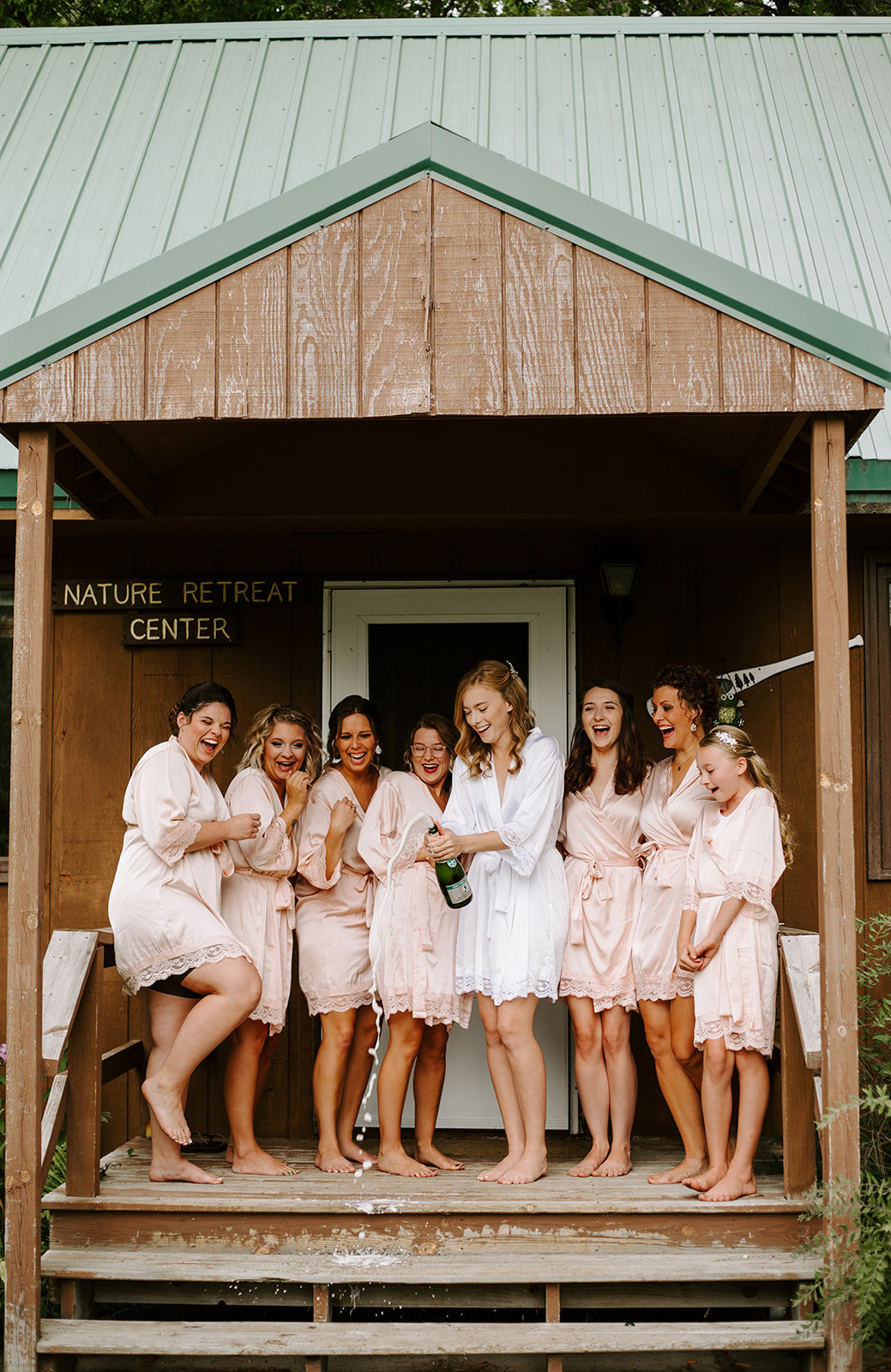 Bride and her bridesmaids popping champagne on the steps of a cabin in their robes on her Minneapolis Wedding day