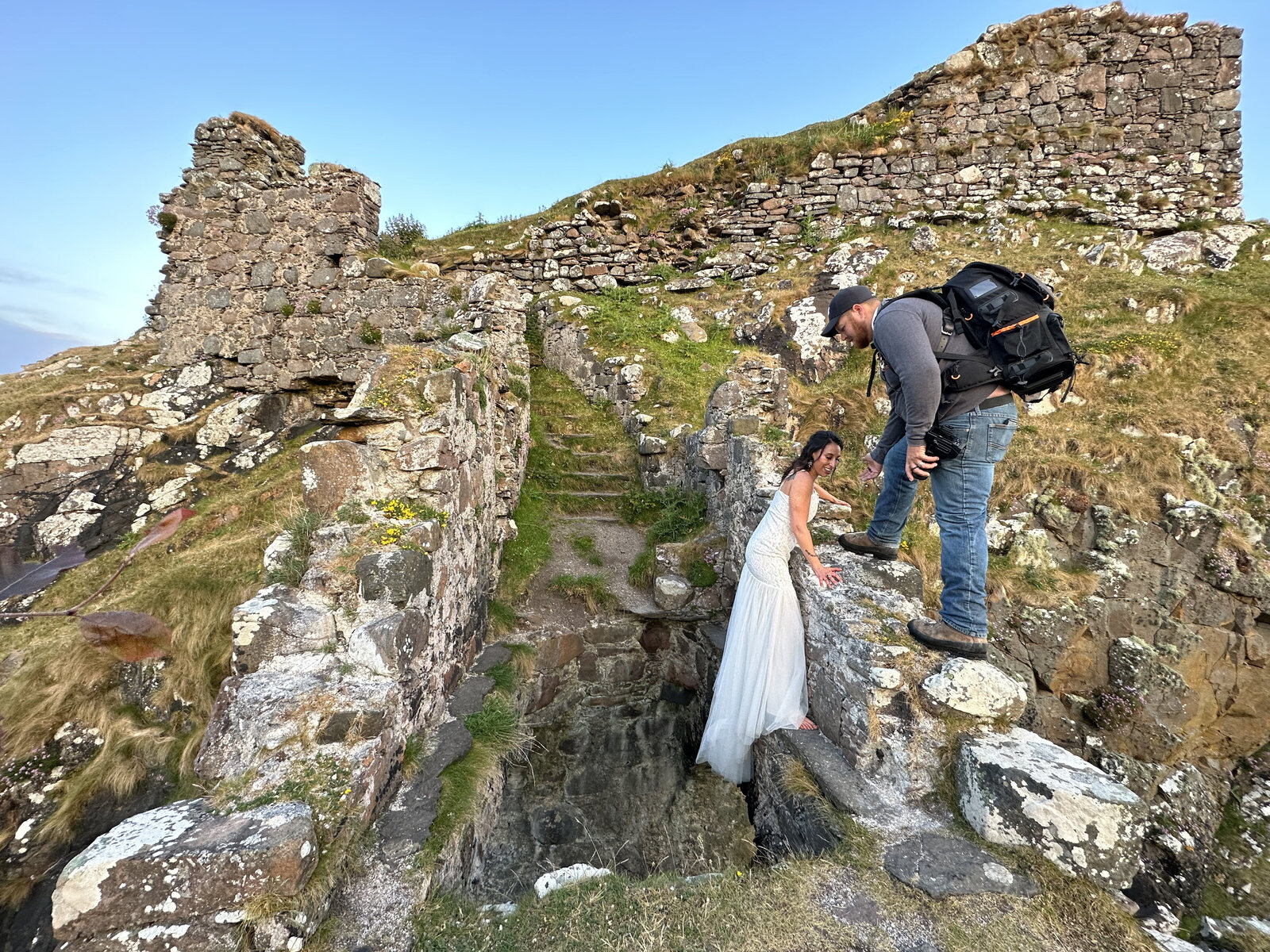 A woman in a white dress climbs ruins as a man with a backpack helps her at an ancient stone site during a Utah desert photography retreat focused on real connection and growth.