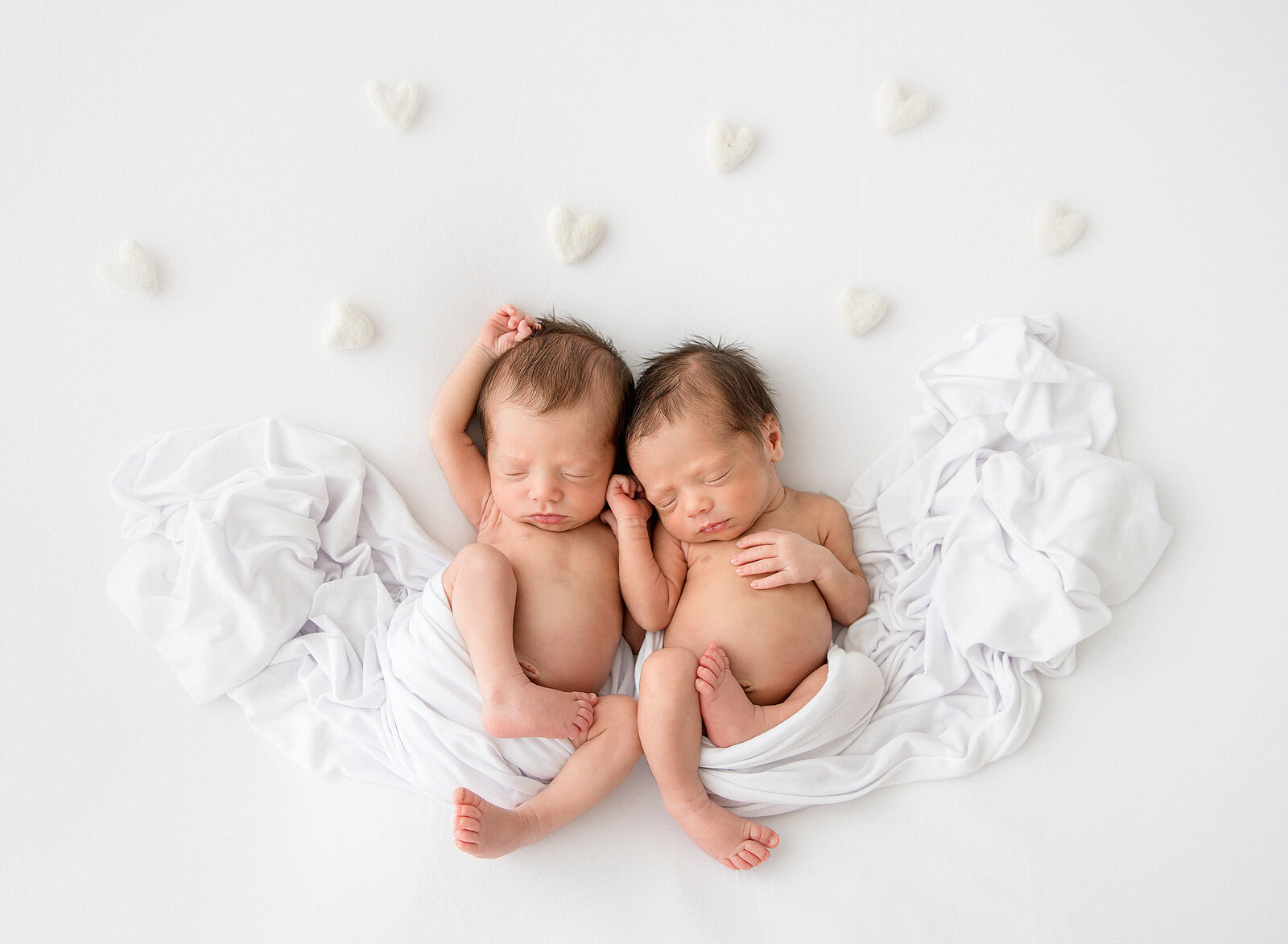 twin newborns with hearts draped around them