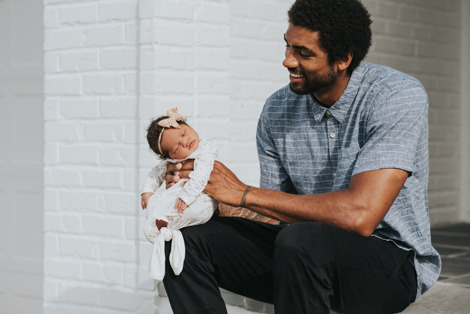 Dad holds newborn baby girl white sleeping on front porch during in-home newborn session by Worth Capturing