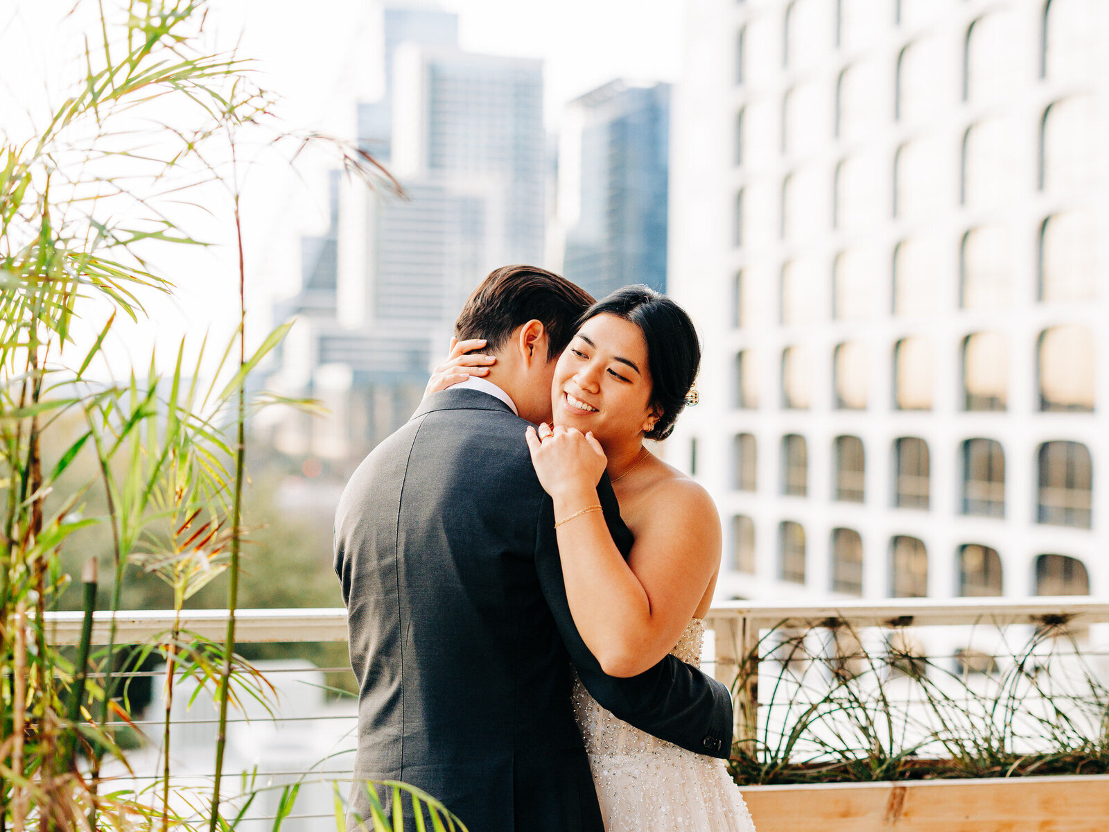 This image features a Vietnamese couple at The Line Hotel in their wedding attire. The groom is wrapping around his bride at the waist as she wraps around him, resting one hand on his shoulder and the other on the back of his neck. The groom is softly kissing her neck. The image was taken by San Antonio Wedding Photographer KD Captures.