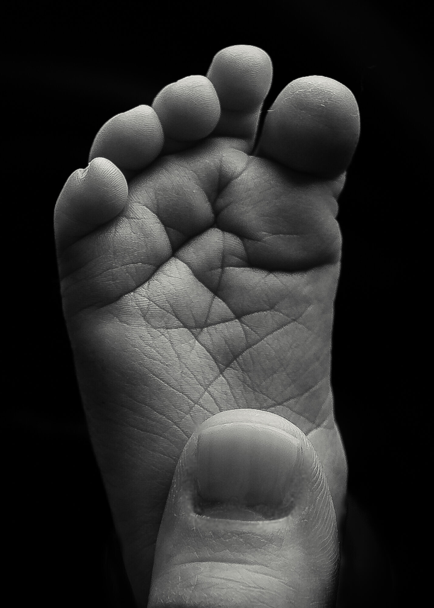 black and white close up of newborn foot with moms thumb