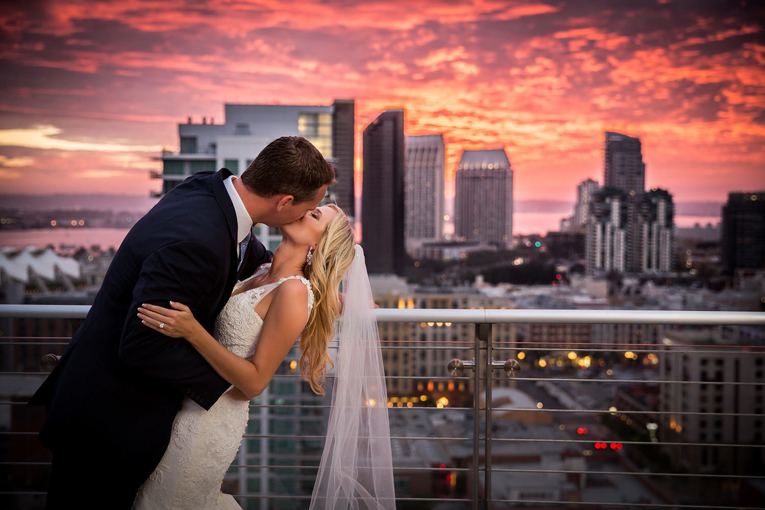 Bride and groom kiss with a surreal sunset over downtown San Diego