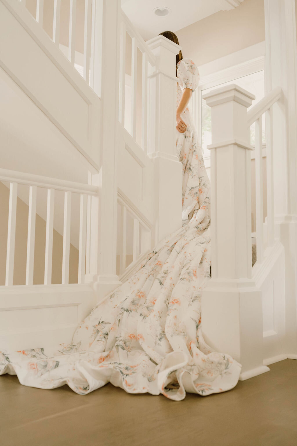 Bride wearing a floral printed wedding dress with a dramatic train walking up a flight of stairs