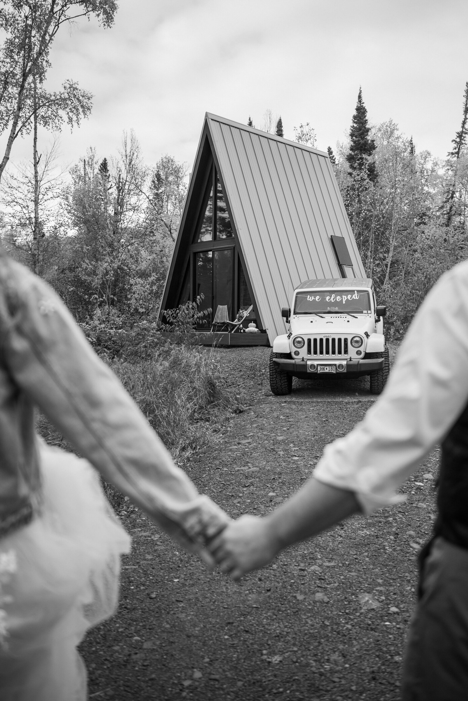 The PNW elopement couples holding hands and look at their A-Frame cabin