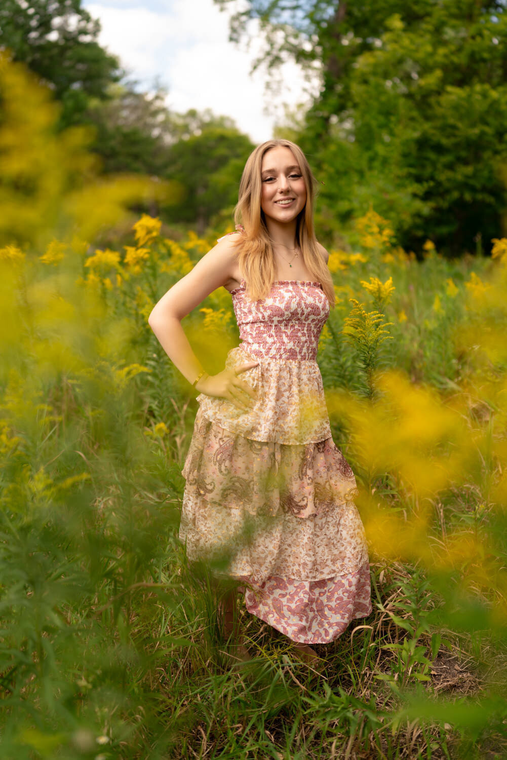 Senior girl stands in a flower field in a pink sundress.