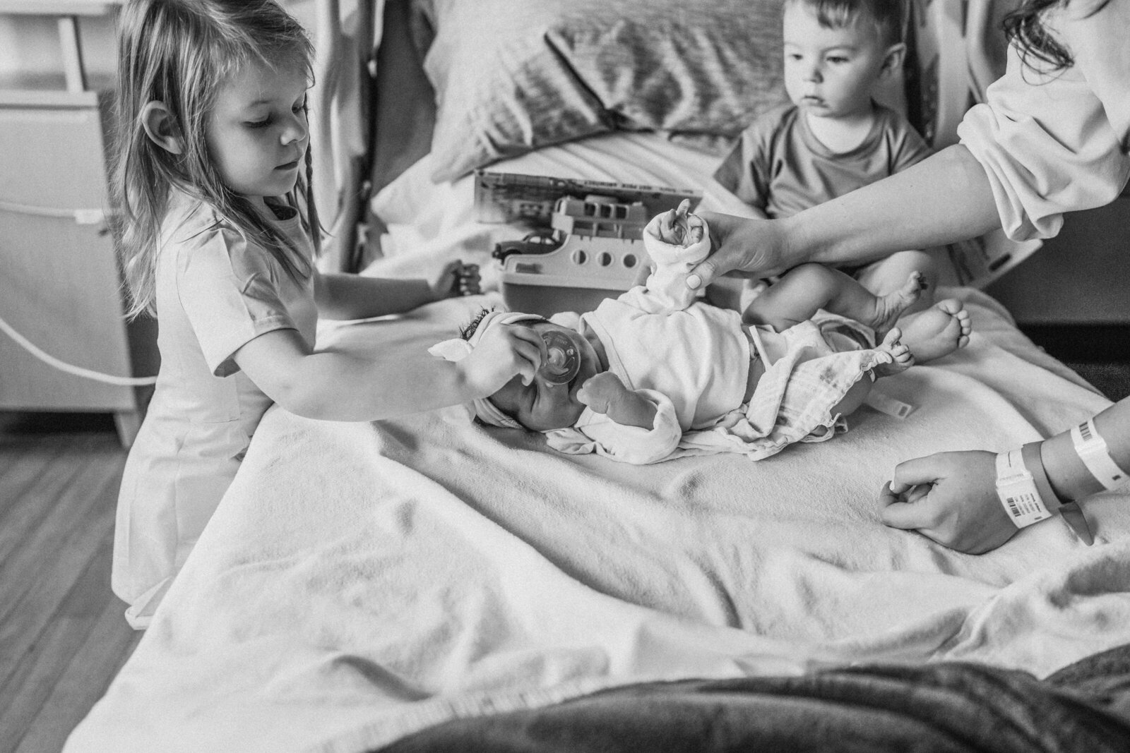 siblings in bed looking at baby