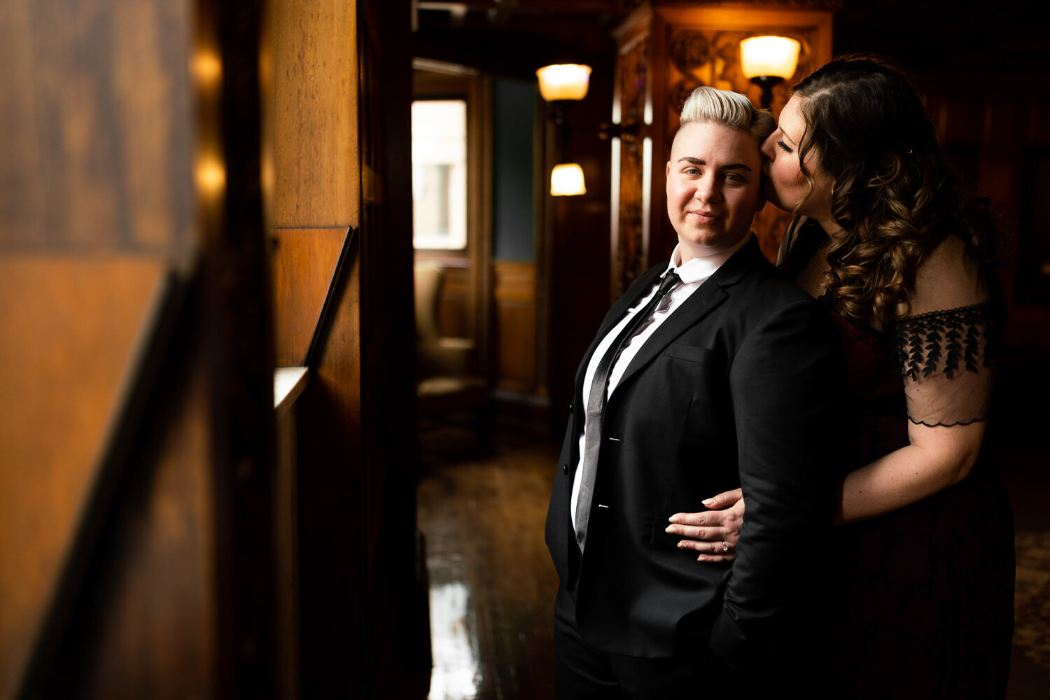 Woman kisses a woman in a suit in front of a window at the Landmark Center in Saint Paul, Minnesota.