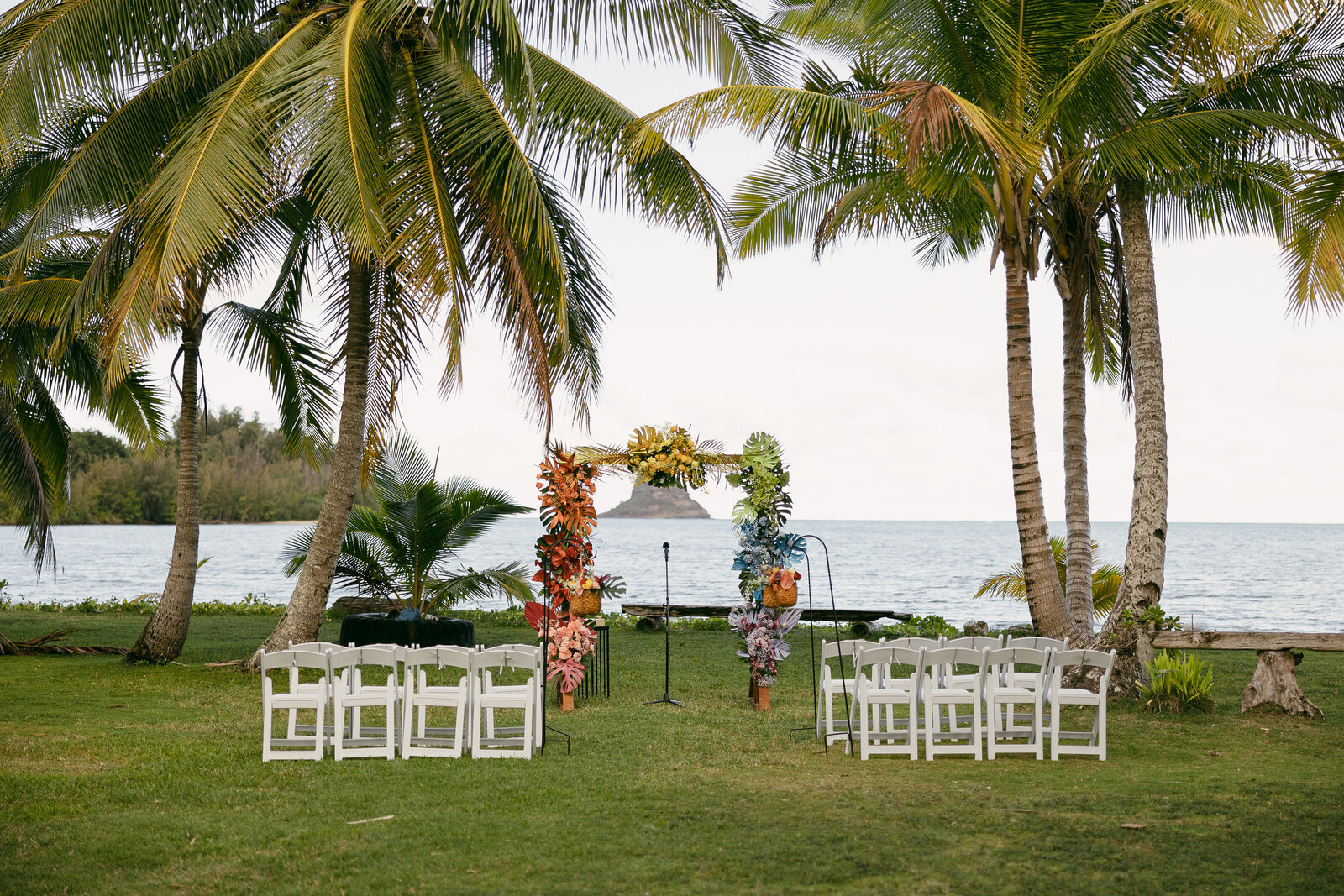 White chairs set up on either side of an aisle with a flower arch at the end.