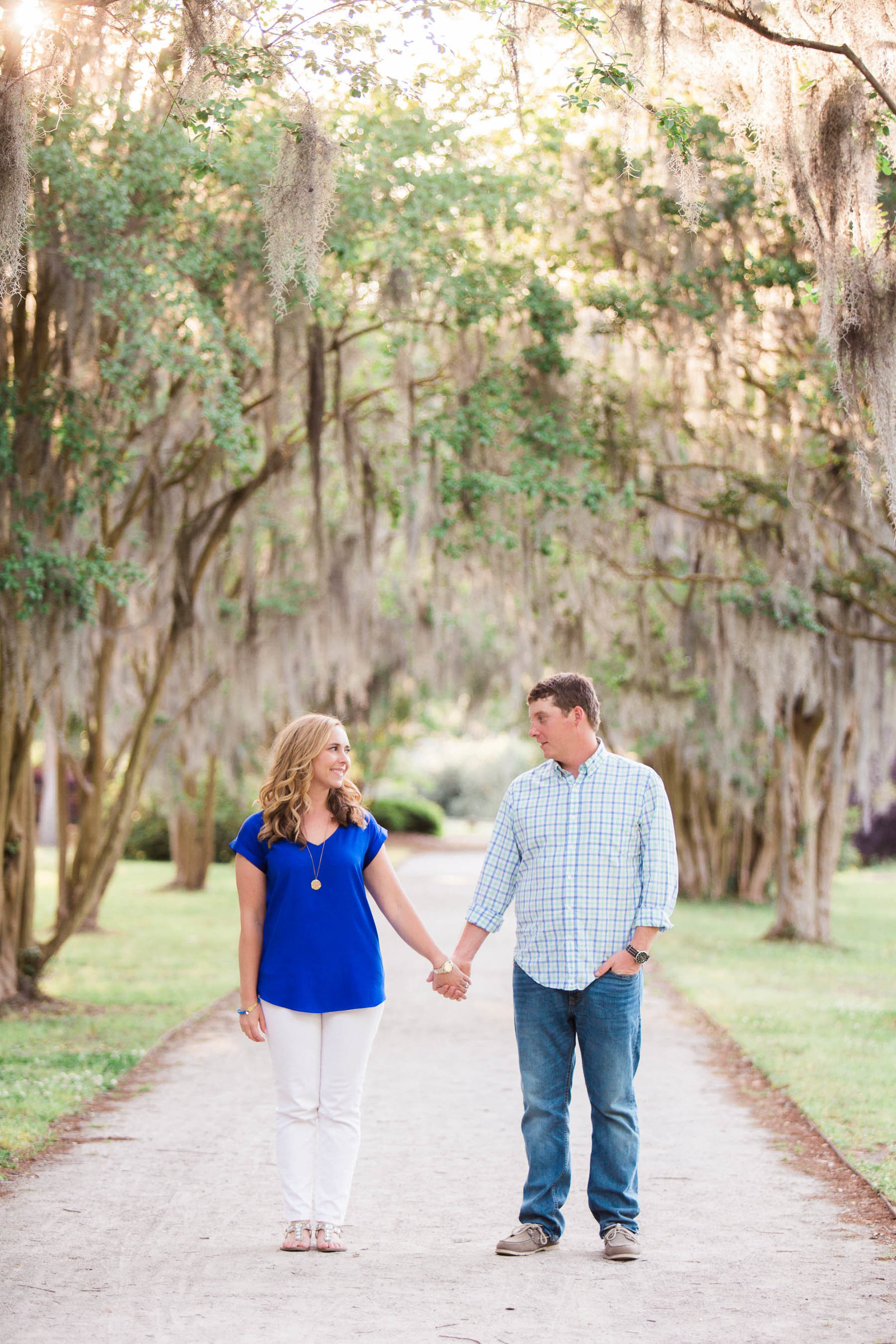 Engaged couple stand in pathway full of trees and spanish moss, Hampton Park, Charleston, South Carolina