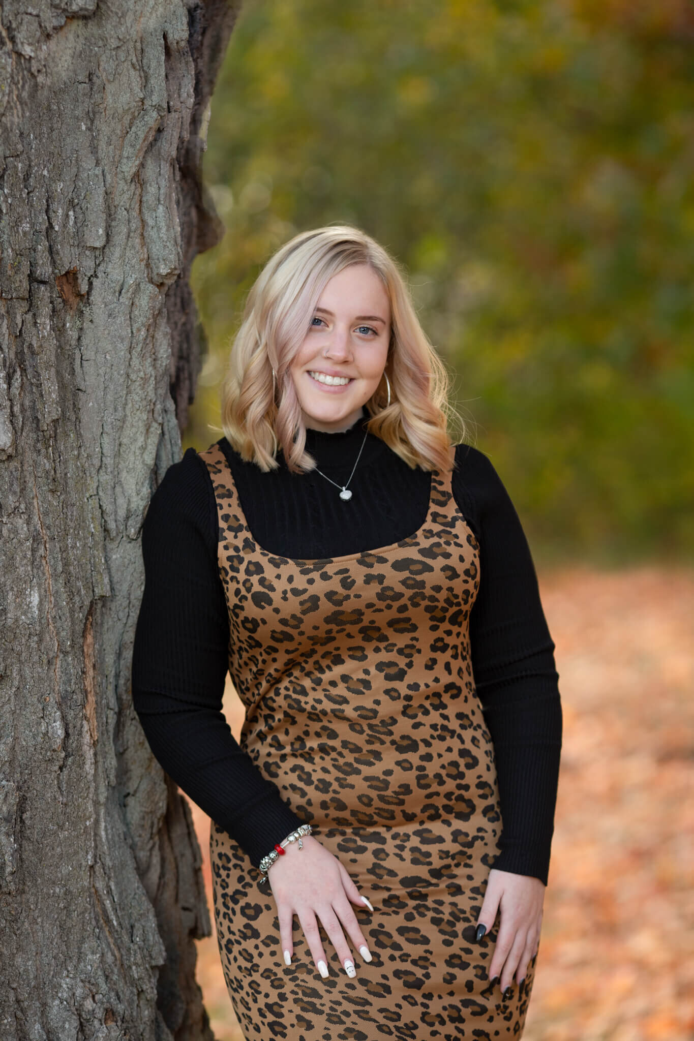 High school senior portrait of girl wearing leopard print dress leaning on a tree