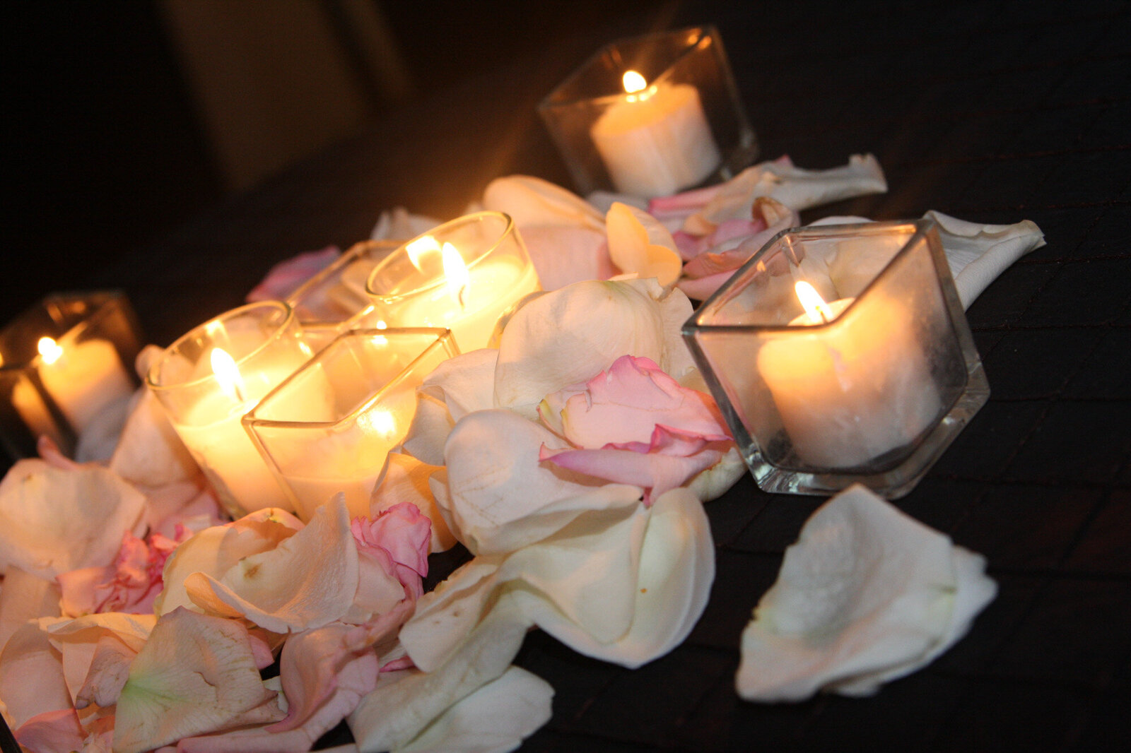 lighted candles in a glass with flower petals surrounding
