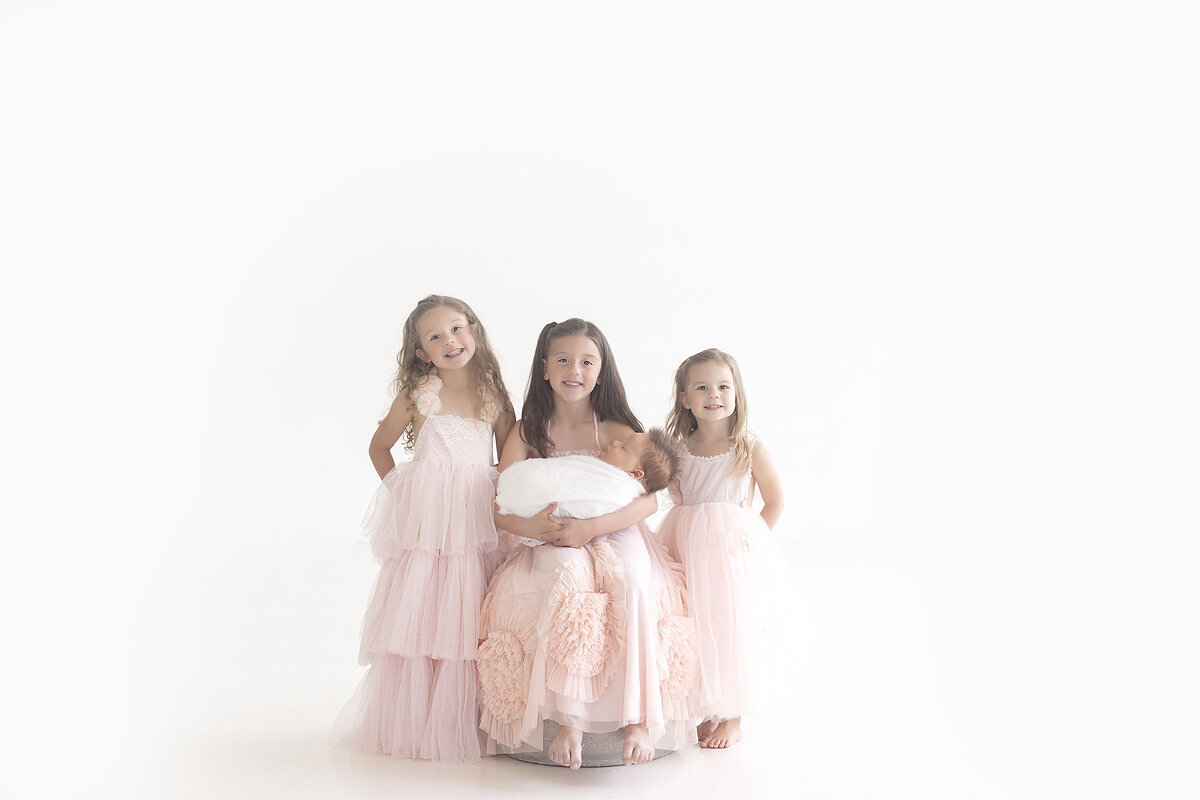 3 young girls holding new baby brother in sibling photos at newborn session.