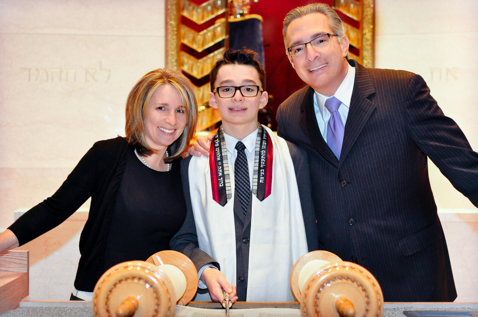 A boy stands at the Bimah with the Torah between mom and dad smiling for a Bellevue Bar and Bat Mitzvah Photography