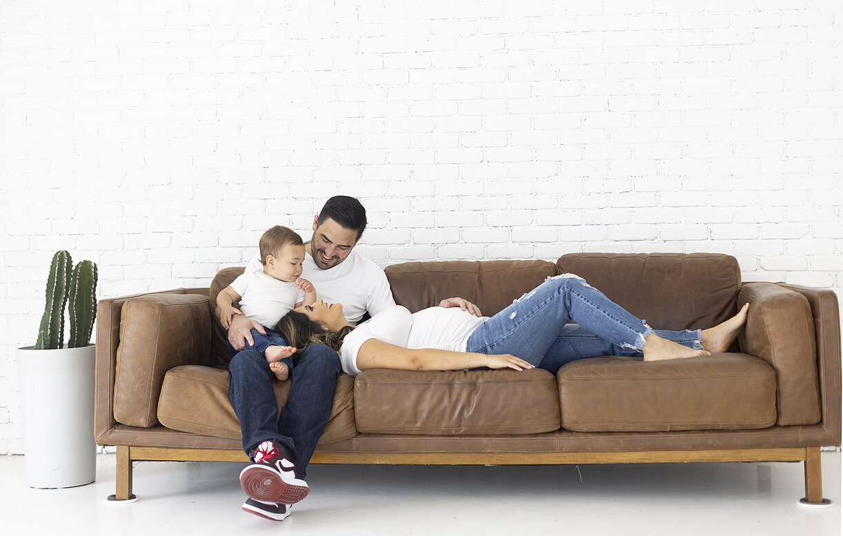 Pregnant mother snuggling with family on leather couch.