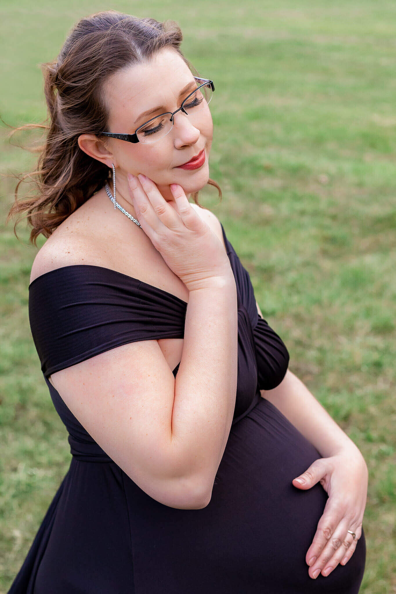 A beautiful pregnant woman in a black dress posing in a field in Chantilly.