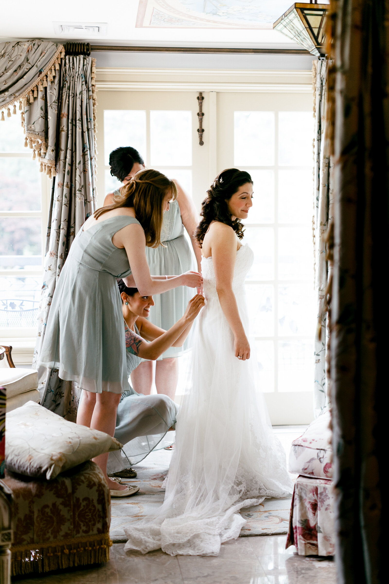bridesmaids helping bride into wedding dress