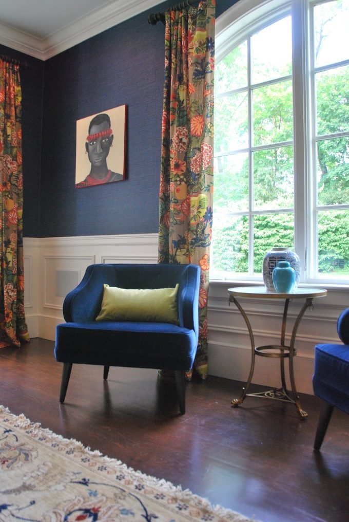Two blue velvet chairs and an accent table in front of an arched window.