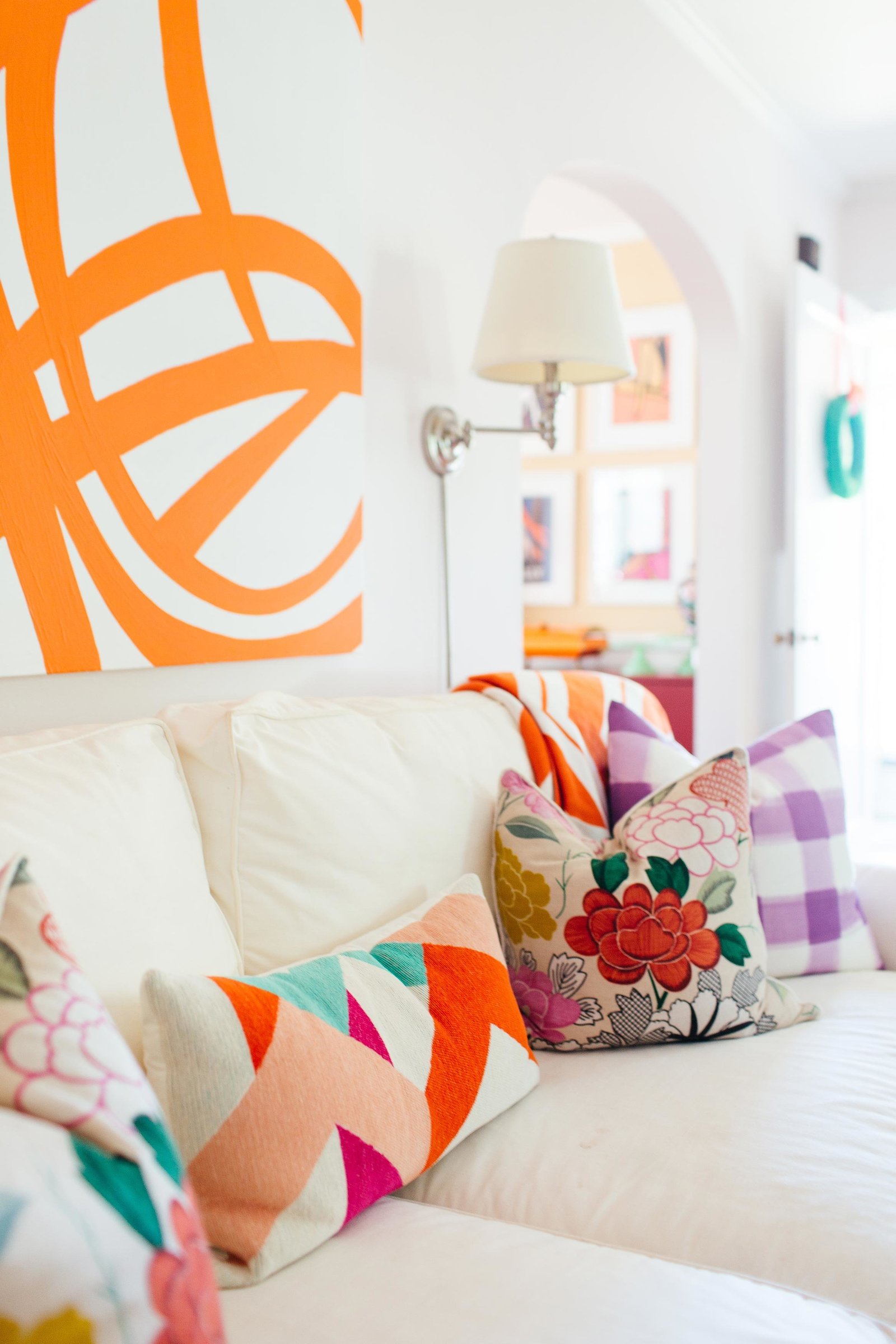 A living room with a large orange and white abstract painting and colorful throw pillows.