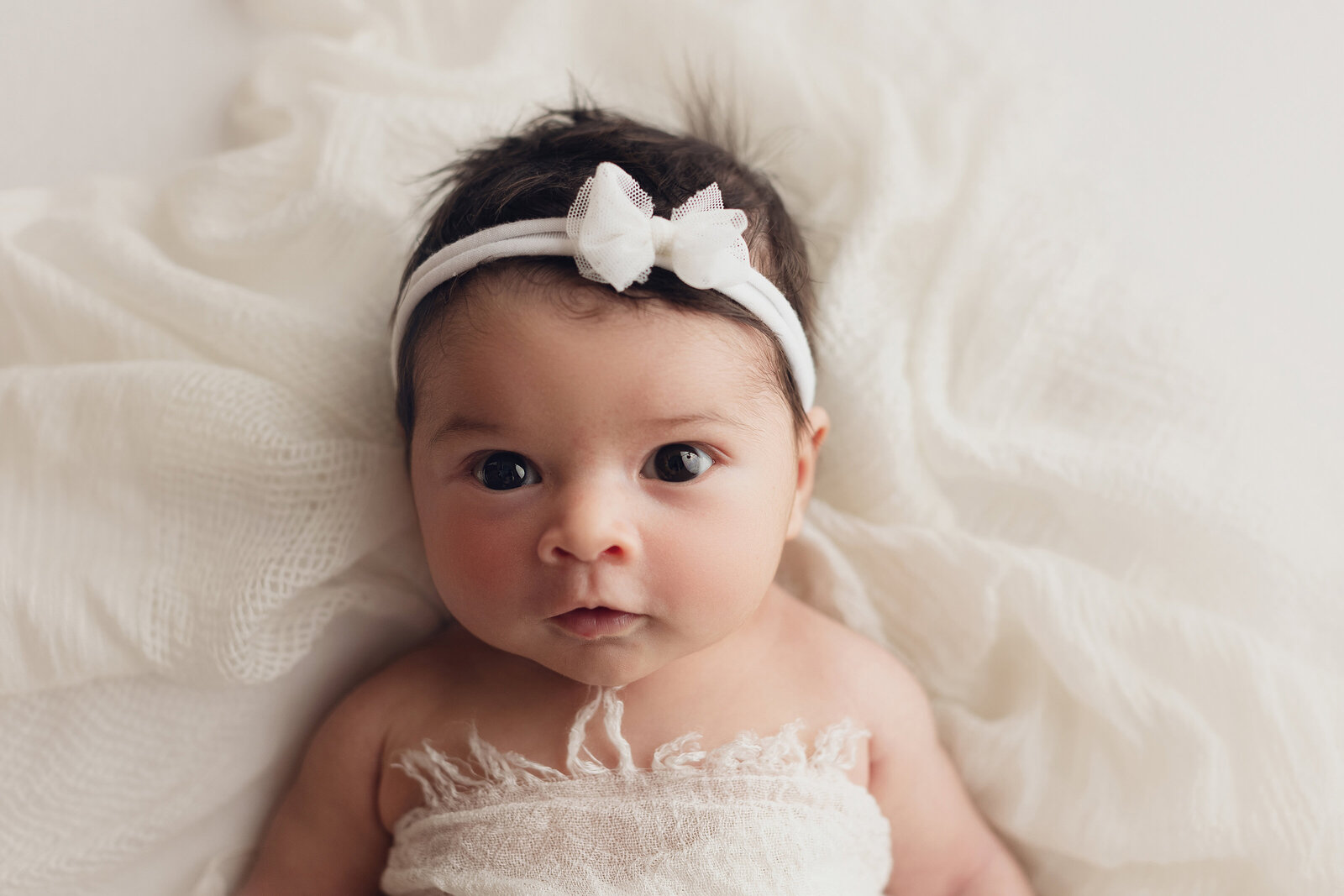 newborn baby girl with white bow on white blanket