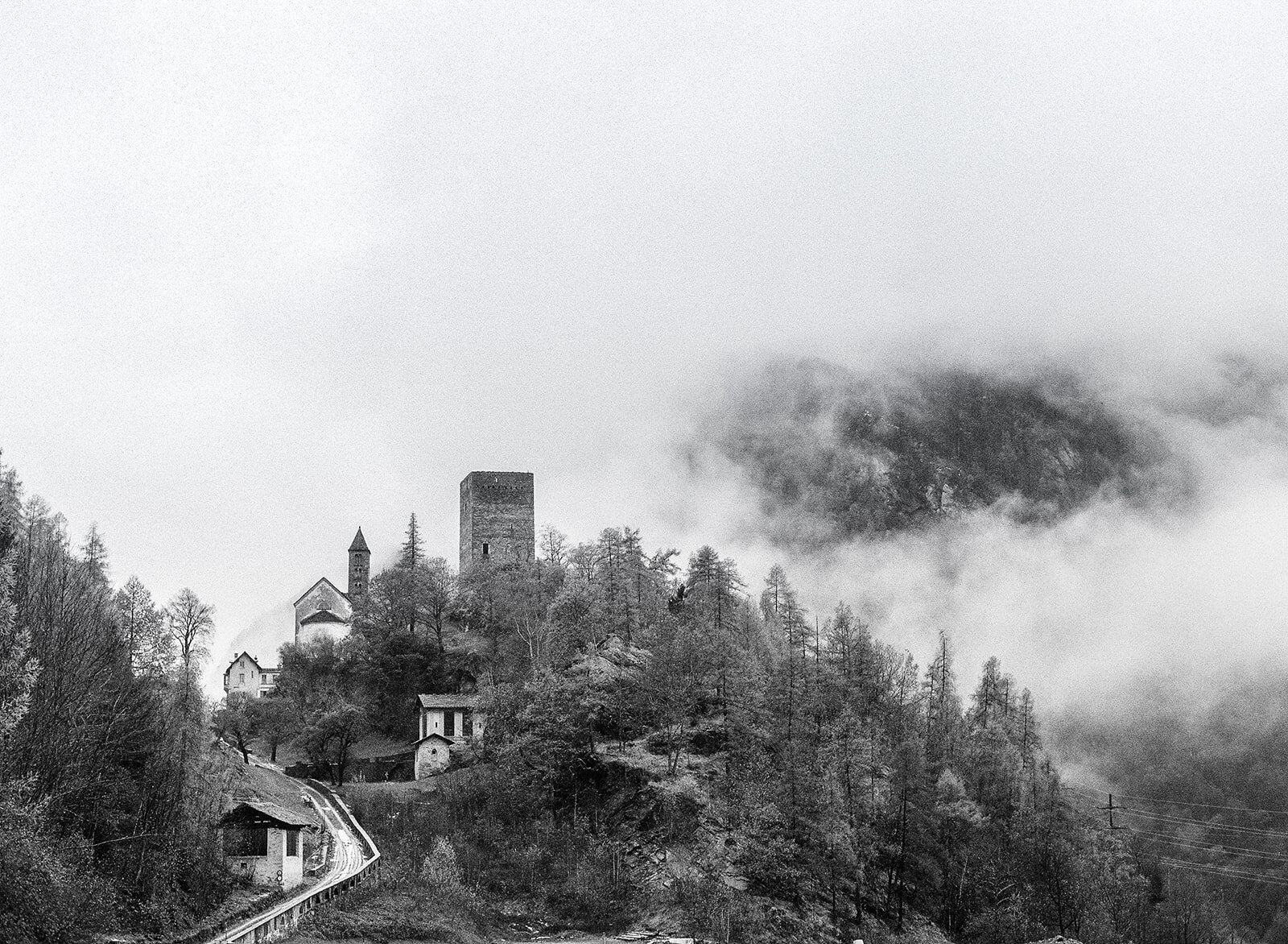 Black and white film photograph of village in the Alps surrounded by fog and mist.