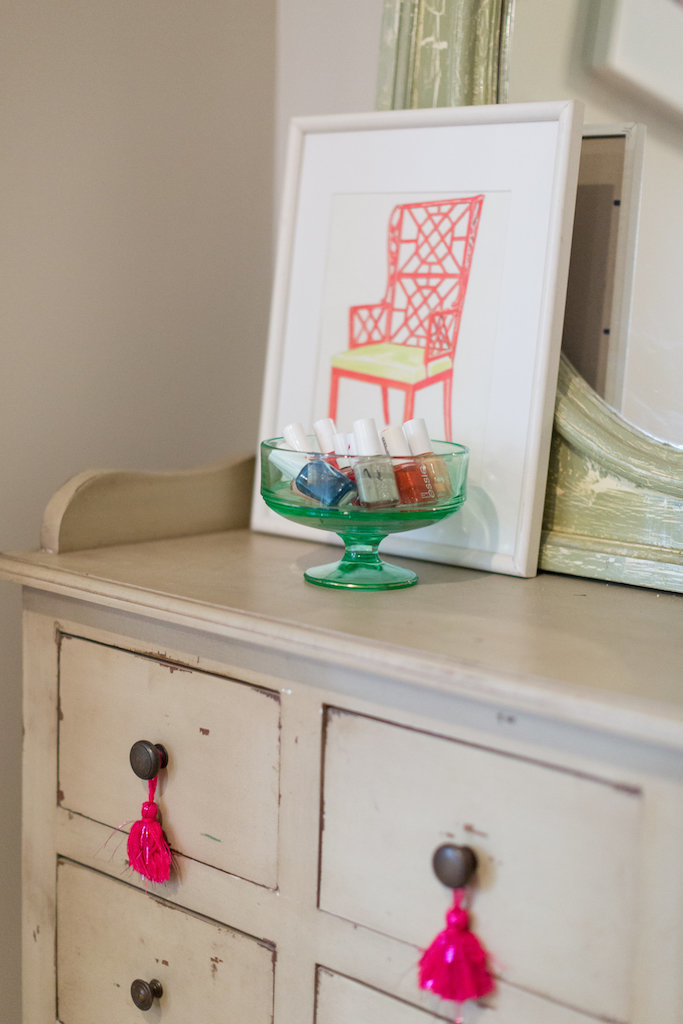 A glass dish and framed art atop a vanity with tassels.