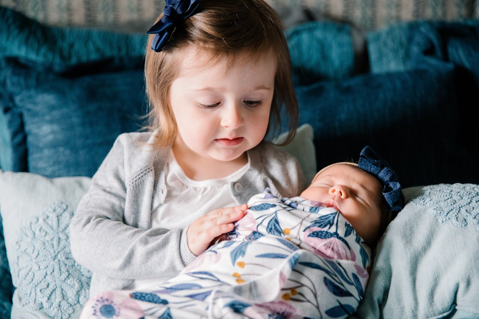 Three year old sister holding newborn sibling during in-home newborn photography session.