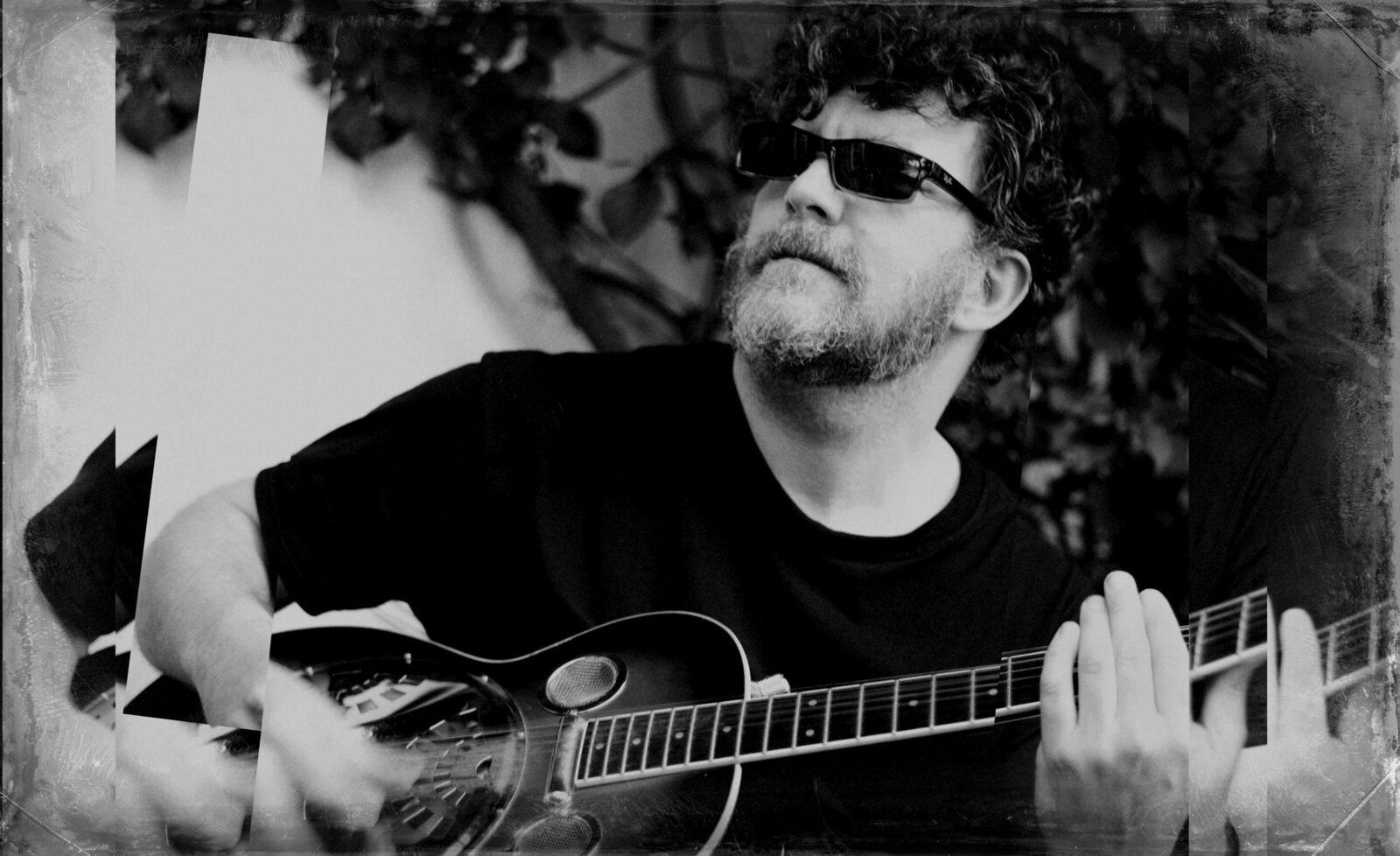 Musician portrait Ben Shepherd black and white wearing sunglasses sitting playing guitar