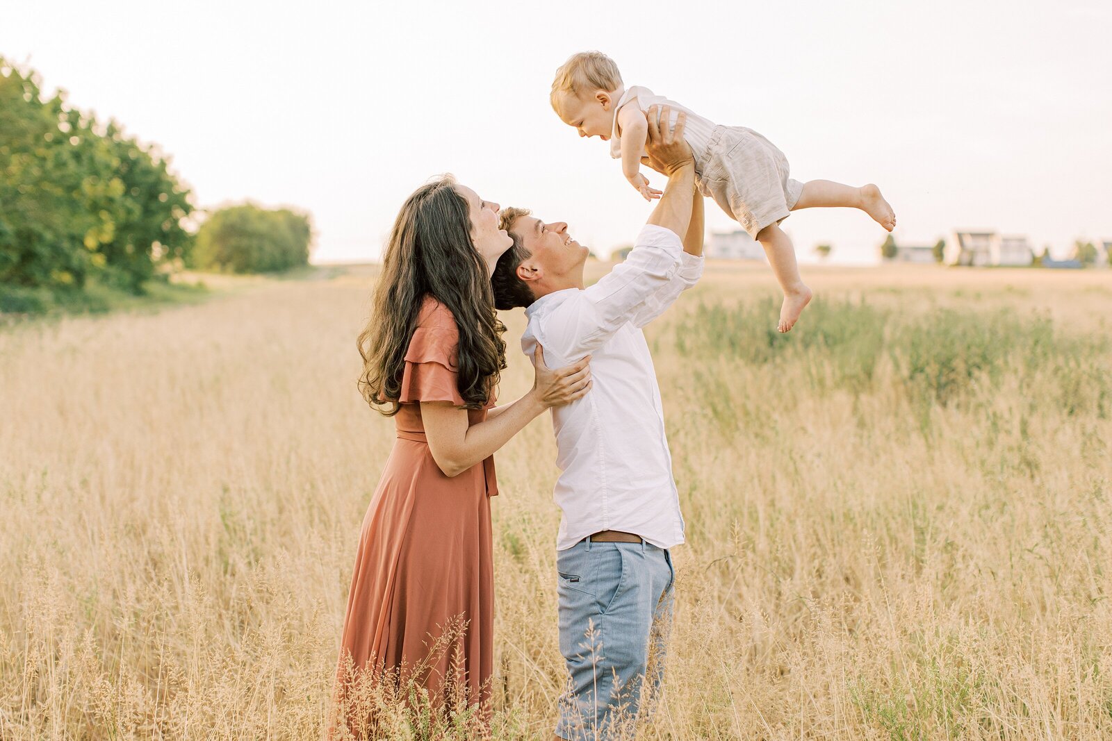 dad flying little boy in field with mom by Philadelphia Family Photographer