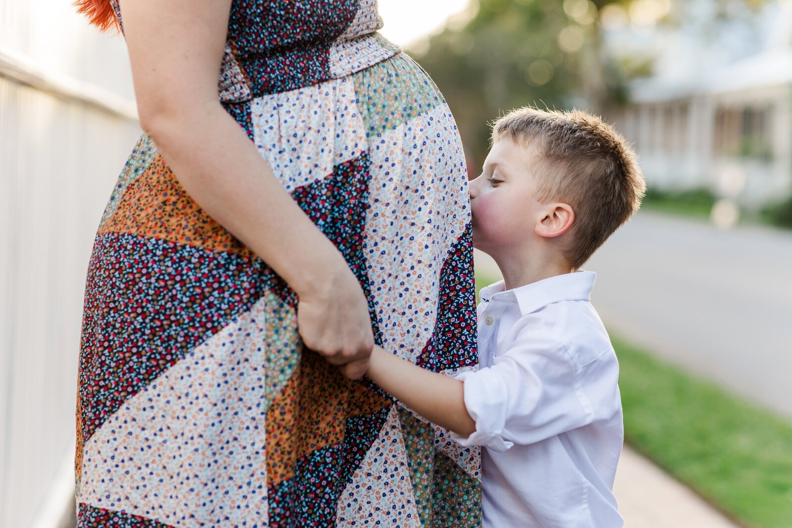 Downtown Pensacola Family Photography session with family of 4. Little boy kissing mom's pregnant belly.