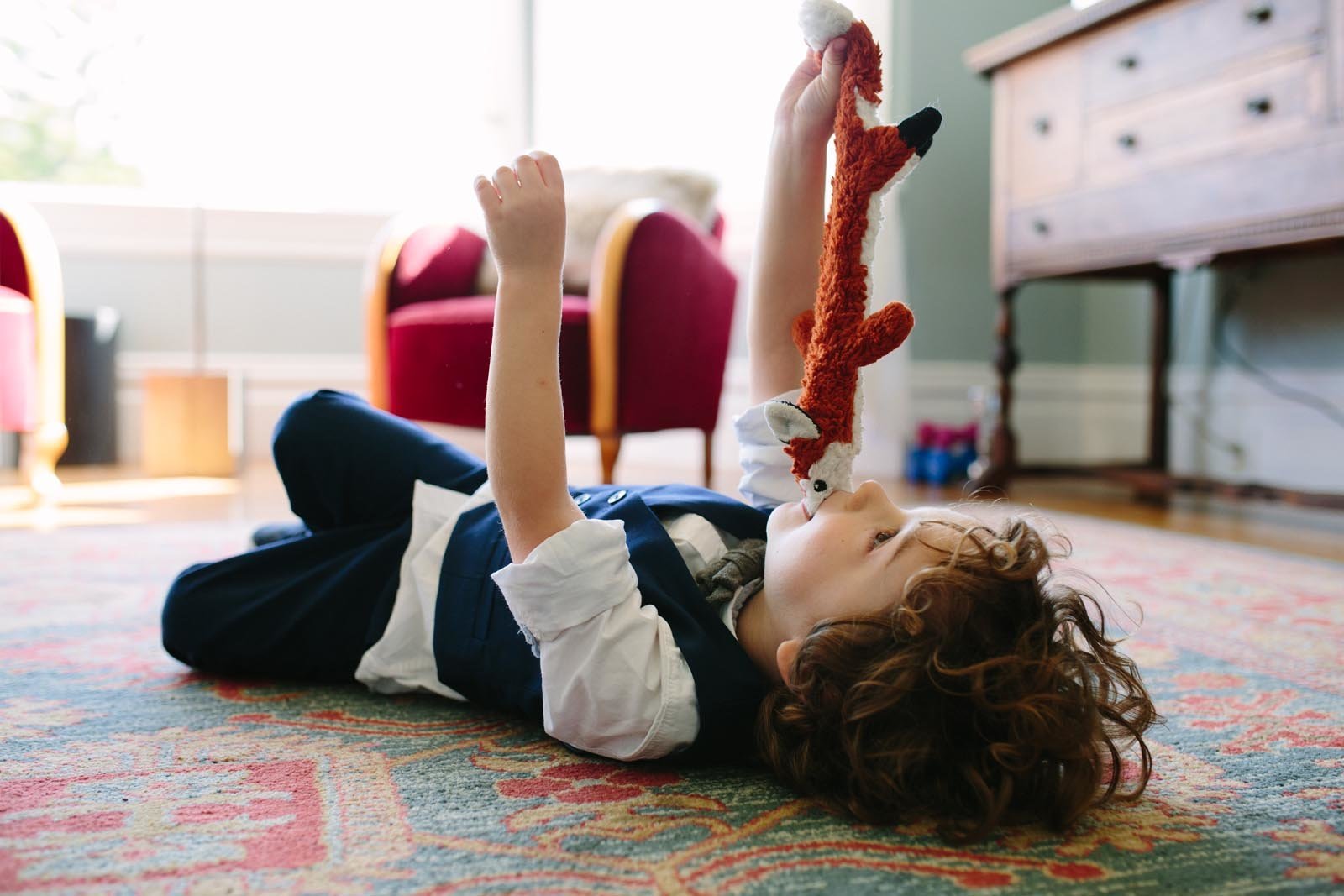 young boy lying on living room rug playing with a dog toy