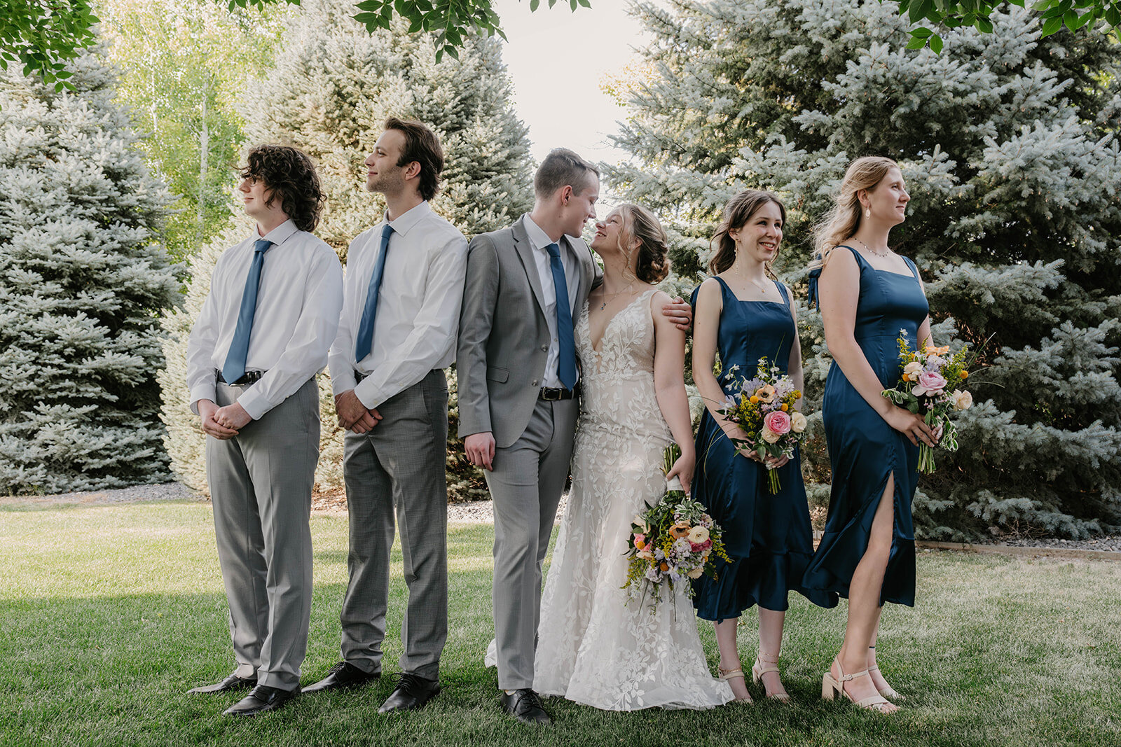 A wedding party poses outdoors during sunset, two men in suits and two women in blue dresses stand with the bride and groom—captured by a Colorado elopement photographer celebrating real connection.