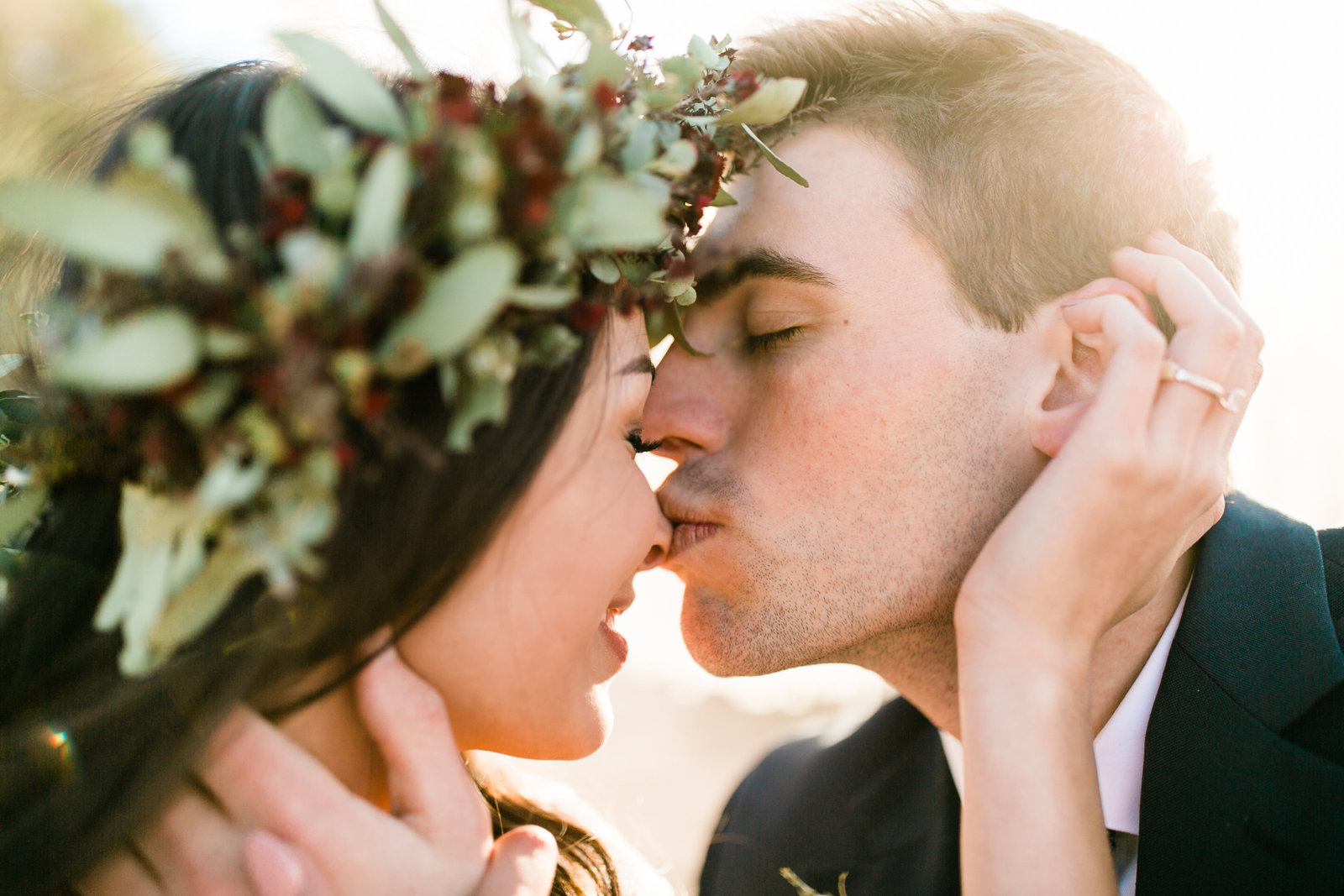 In joshua tree the groom leans in to kiss the brides nose. Sunlight pours over them at sunset.