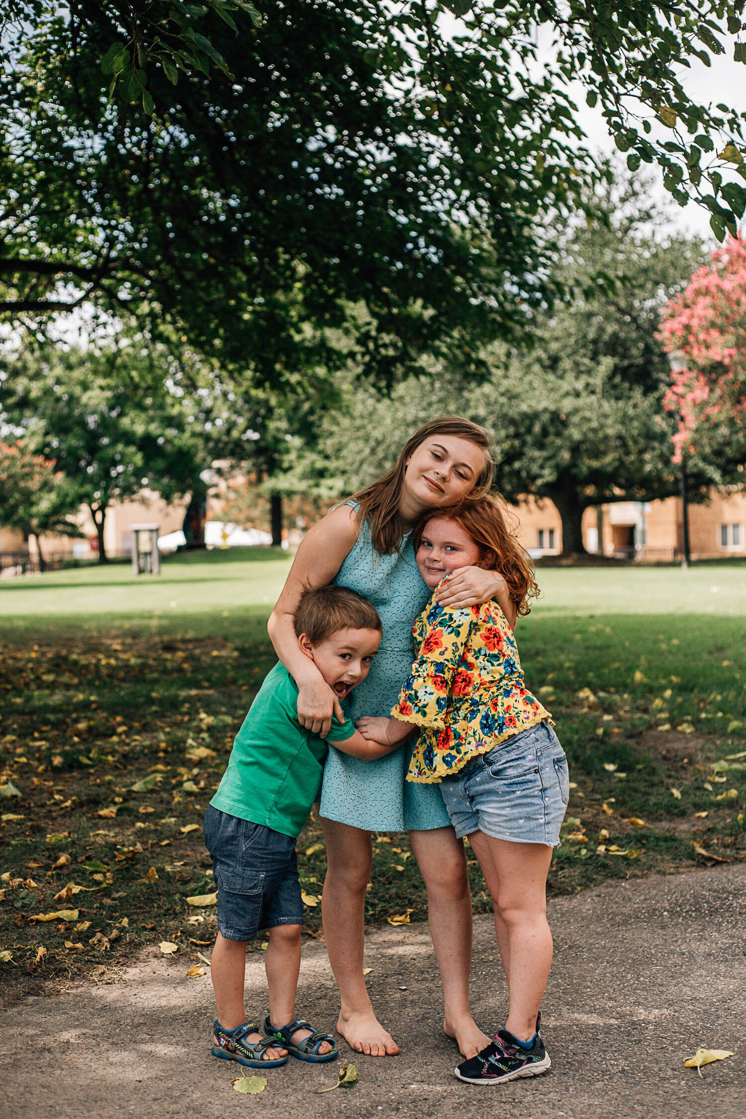 Hampton Roads photographers family photo of three young siblings standing on a sidewalk huggin each other during during summer family photos in Virginia