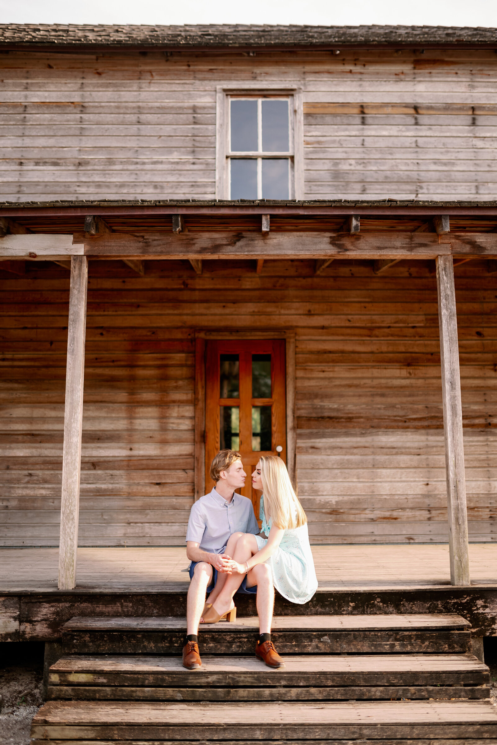 engaged couple sitting together on the steps of a historic house facing each other about to kiss