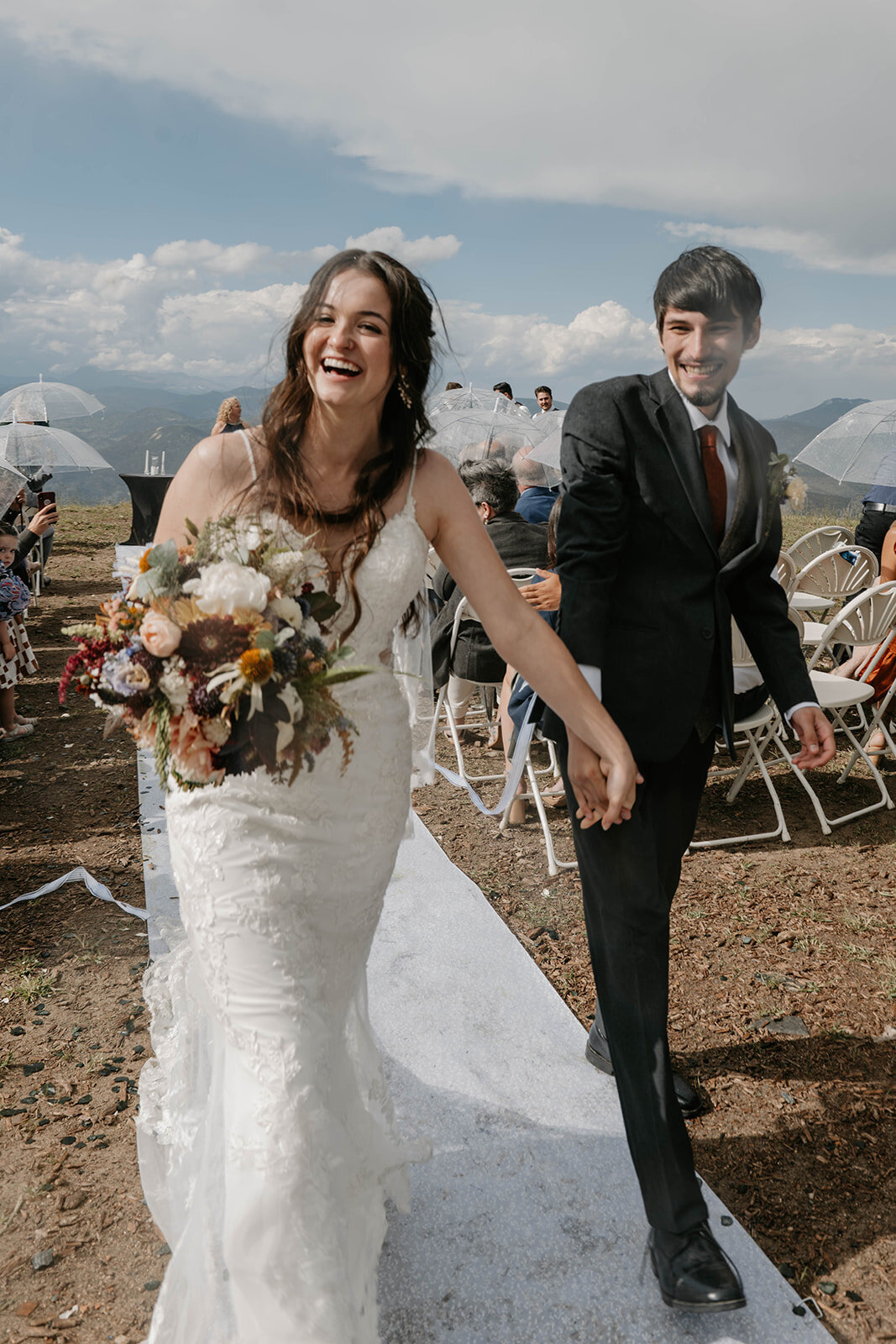 Bride and groom holding hands, smiling, and walking down the aisle during a Colorado wildflower elopement—candid wedding photography at golden hour beautifully capturing their real connection.