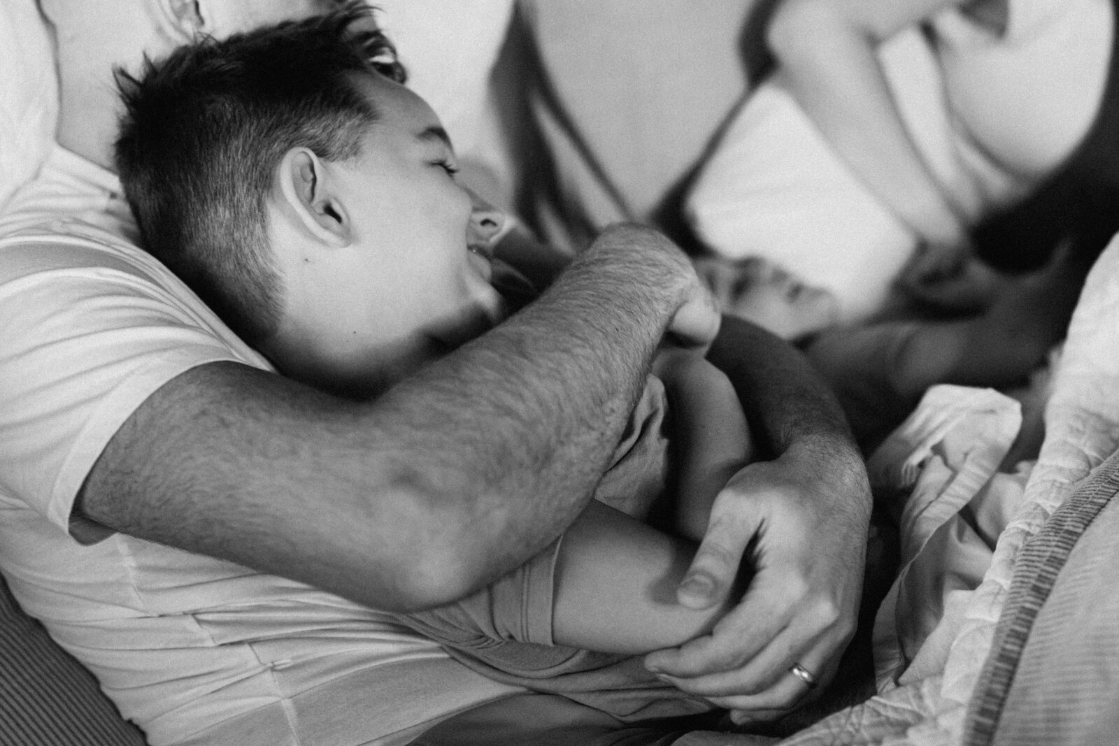 A little boy lays against his dad's chest while dad's arms wrap tightly around him
