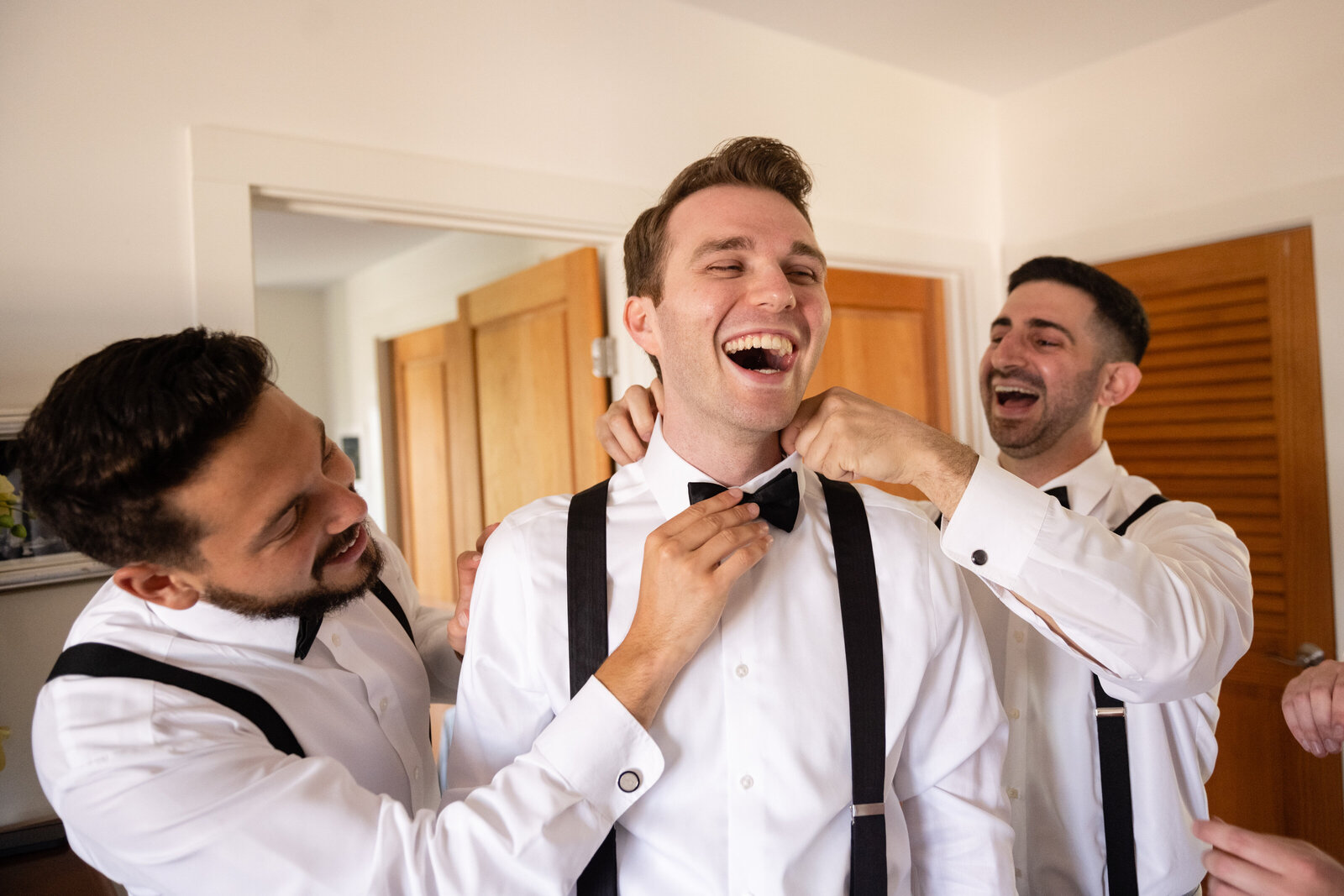 groomsmen help groom get dressed