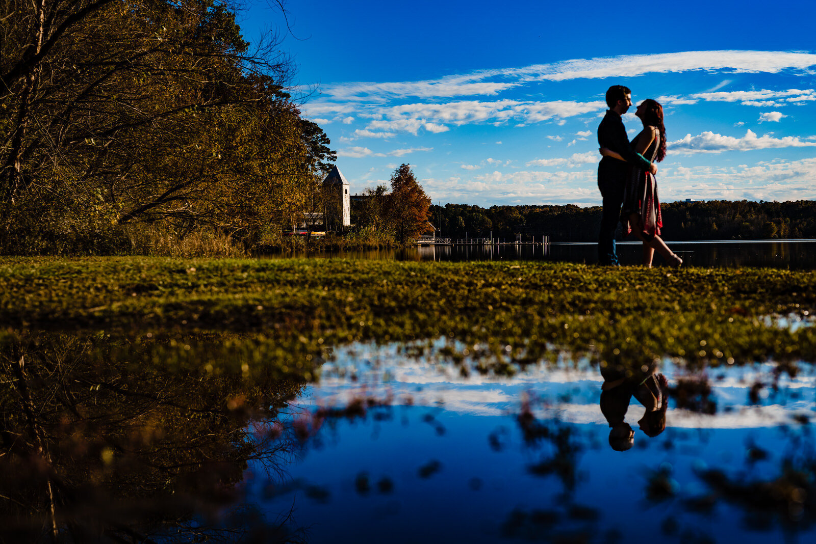 Couple poses next to Lake Crabtree during a Raleigh engagement photo session