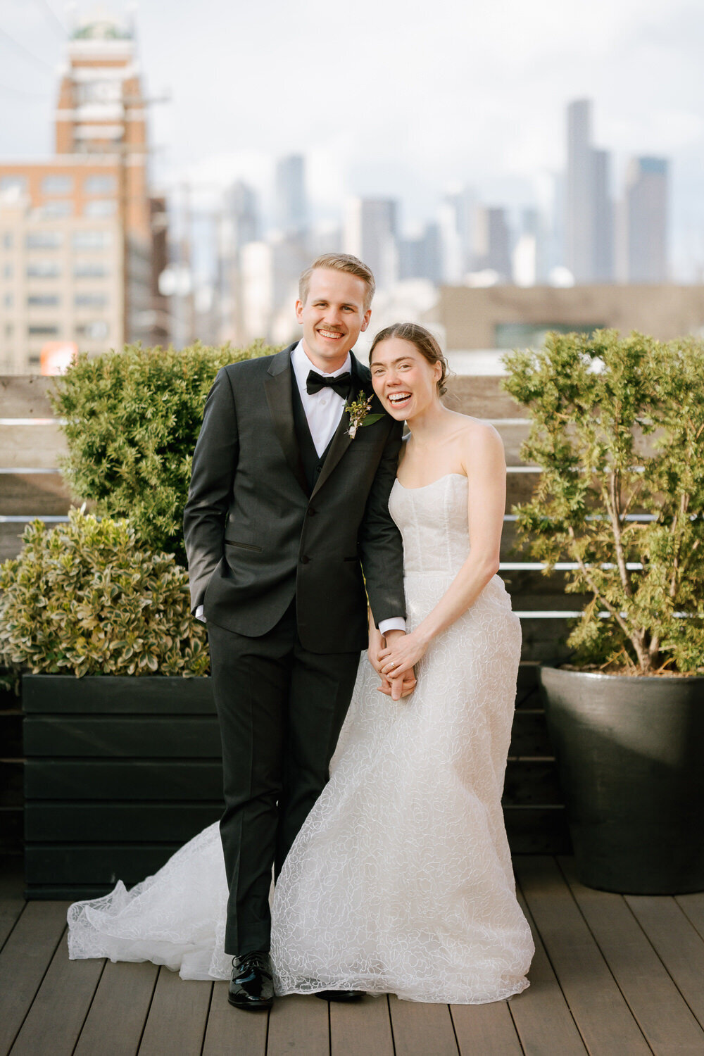 Bride and groom hold hands and smile with the Seattle skyline behind them