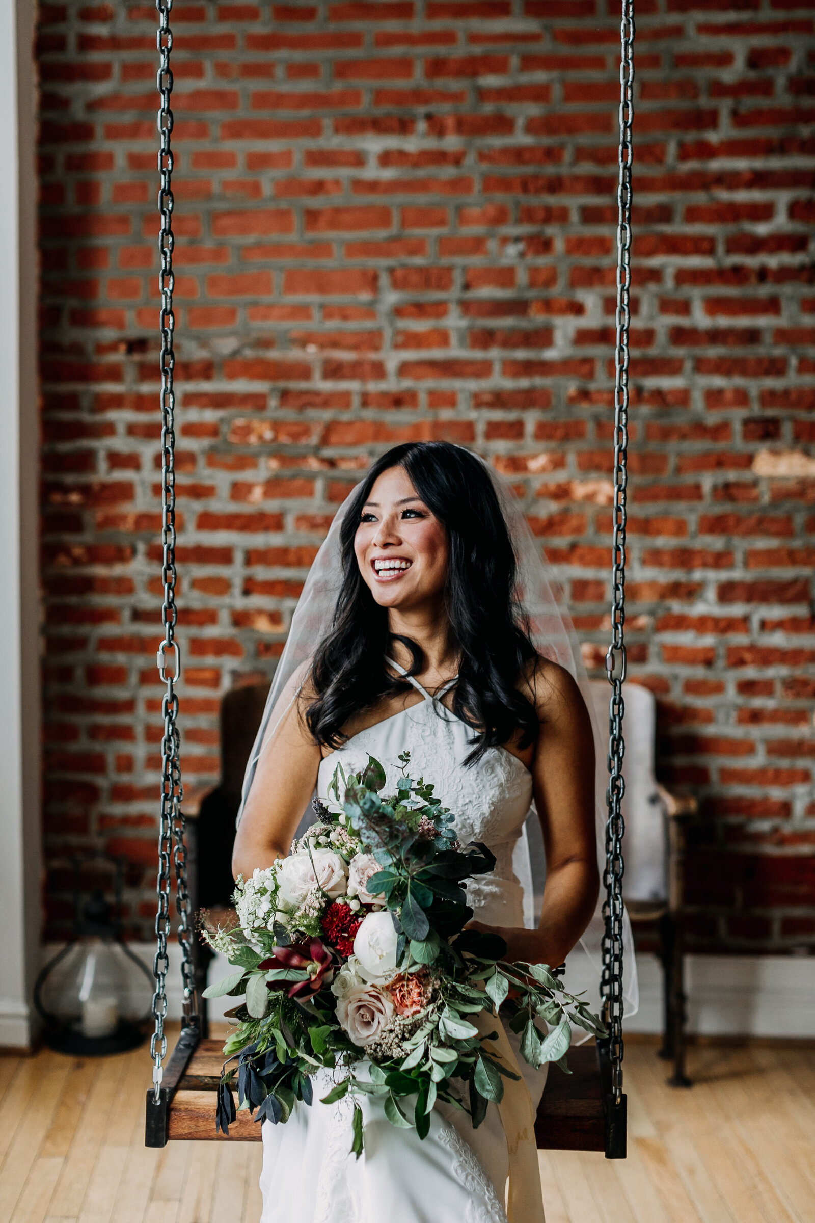 bride with bouquet sitting on swing with brick wall