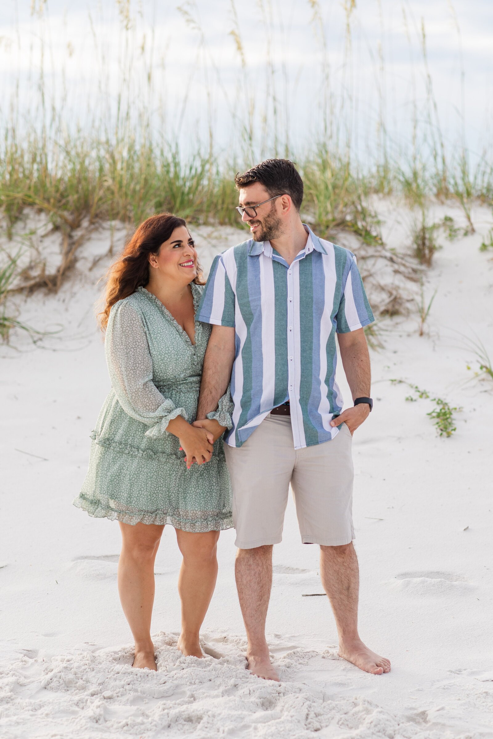 Pensacola Beach vacation family photo session . Mom and dad  holding hands in front of sand dunes.