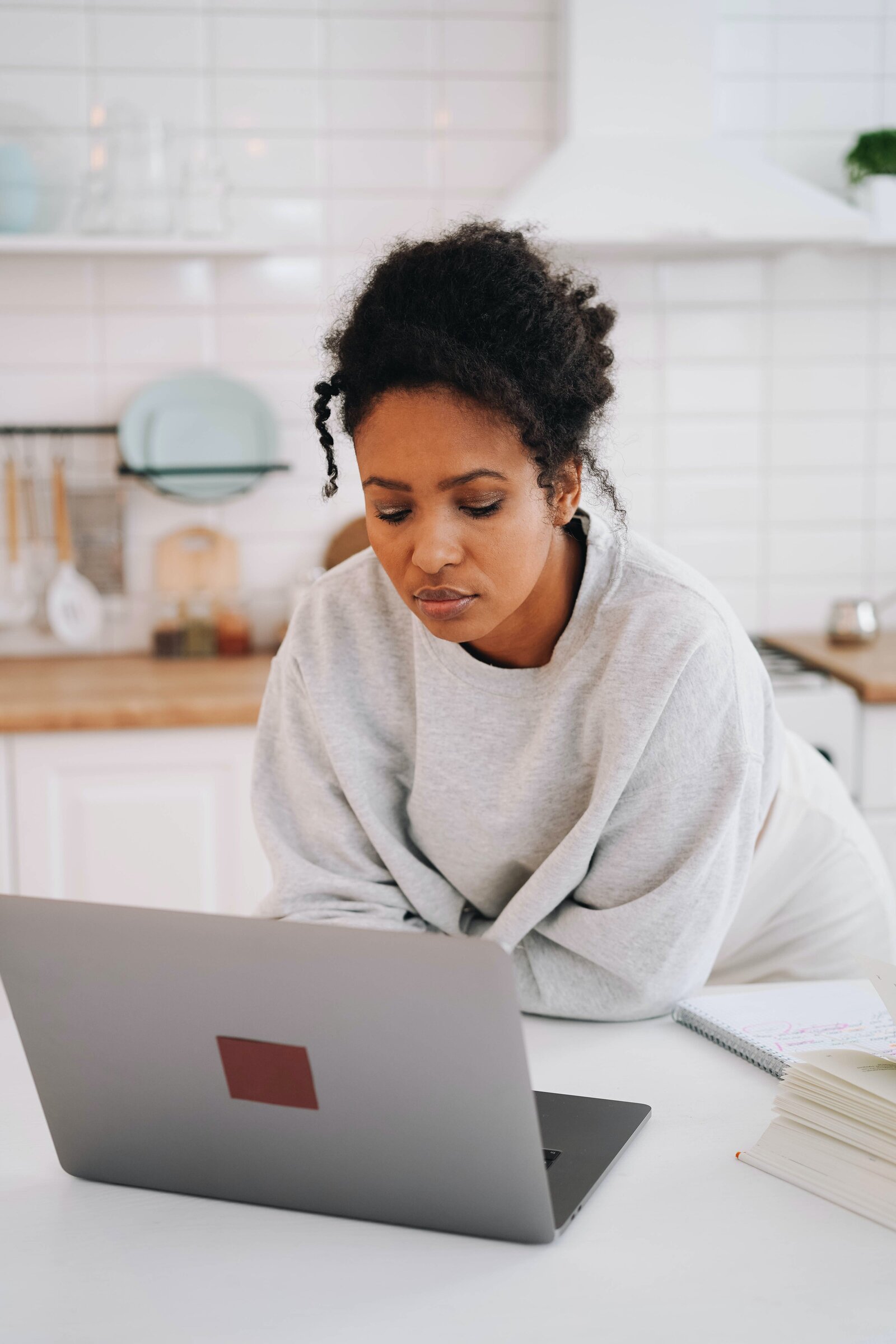 Woman leaning on kitchen counter looking at laptop.