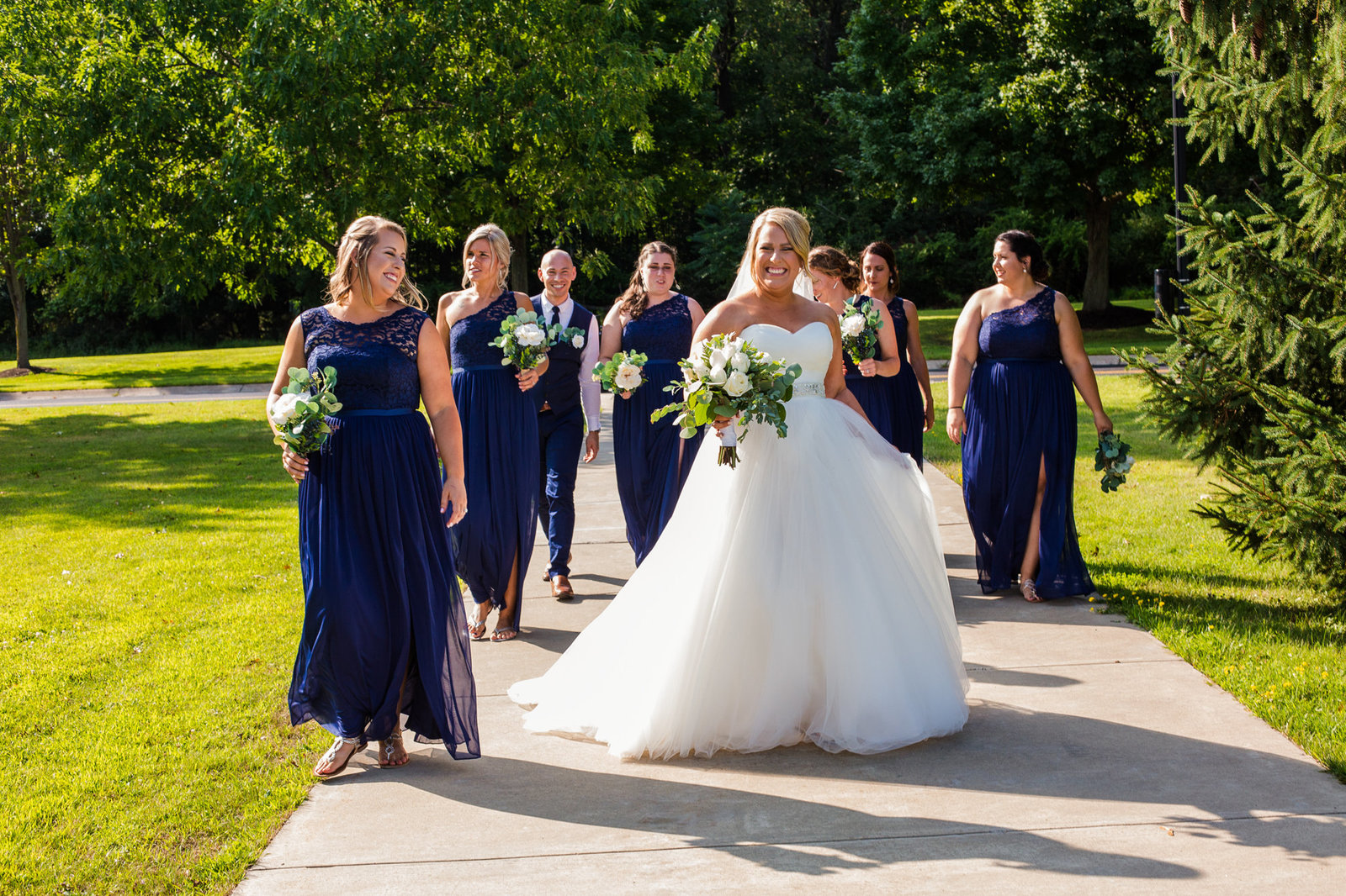Bride walks with her bridal party along a path on the campus of Edinboro University