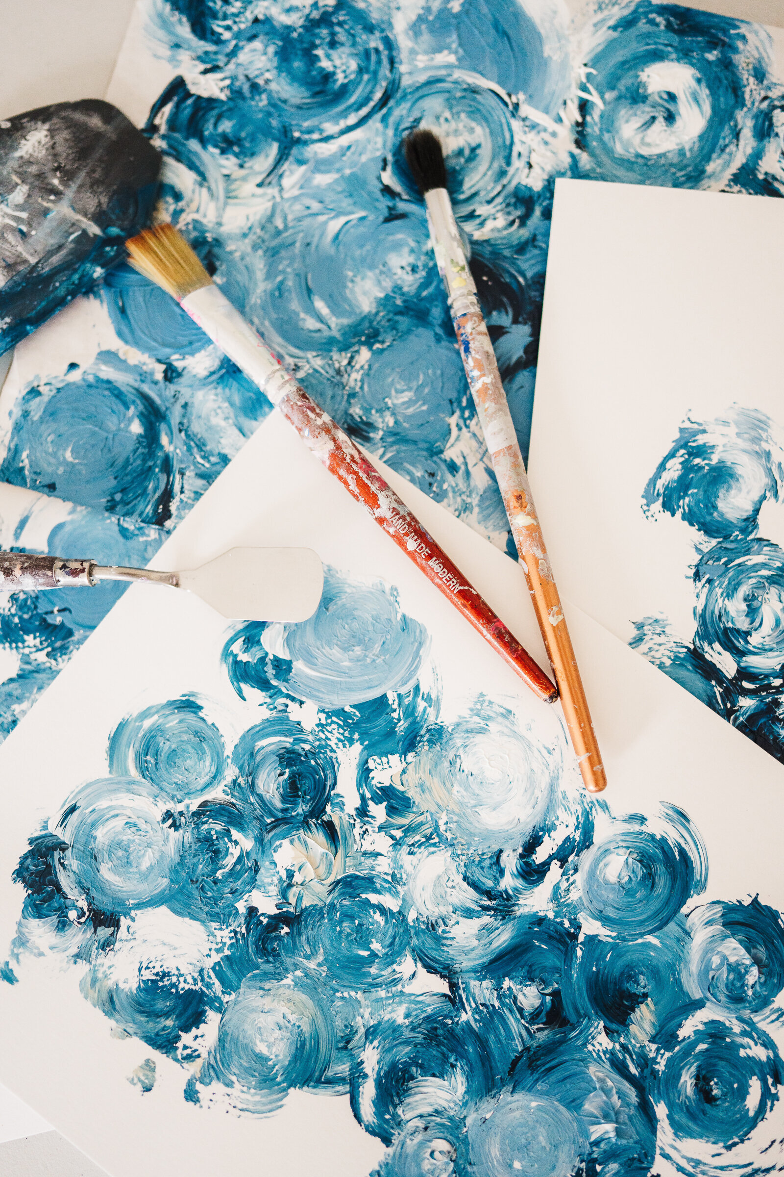 paintbrushes lie on top of white and blue painted paper