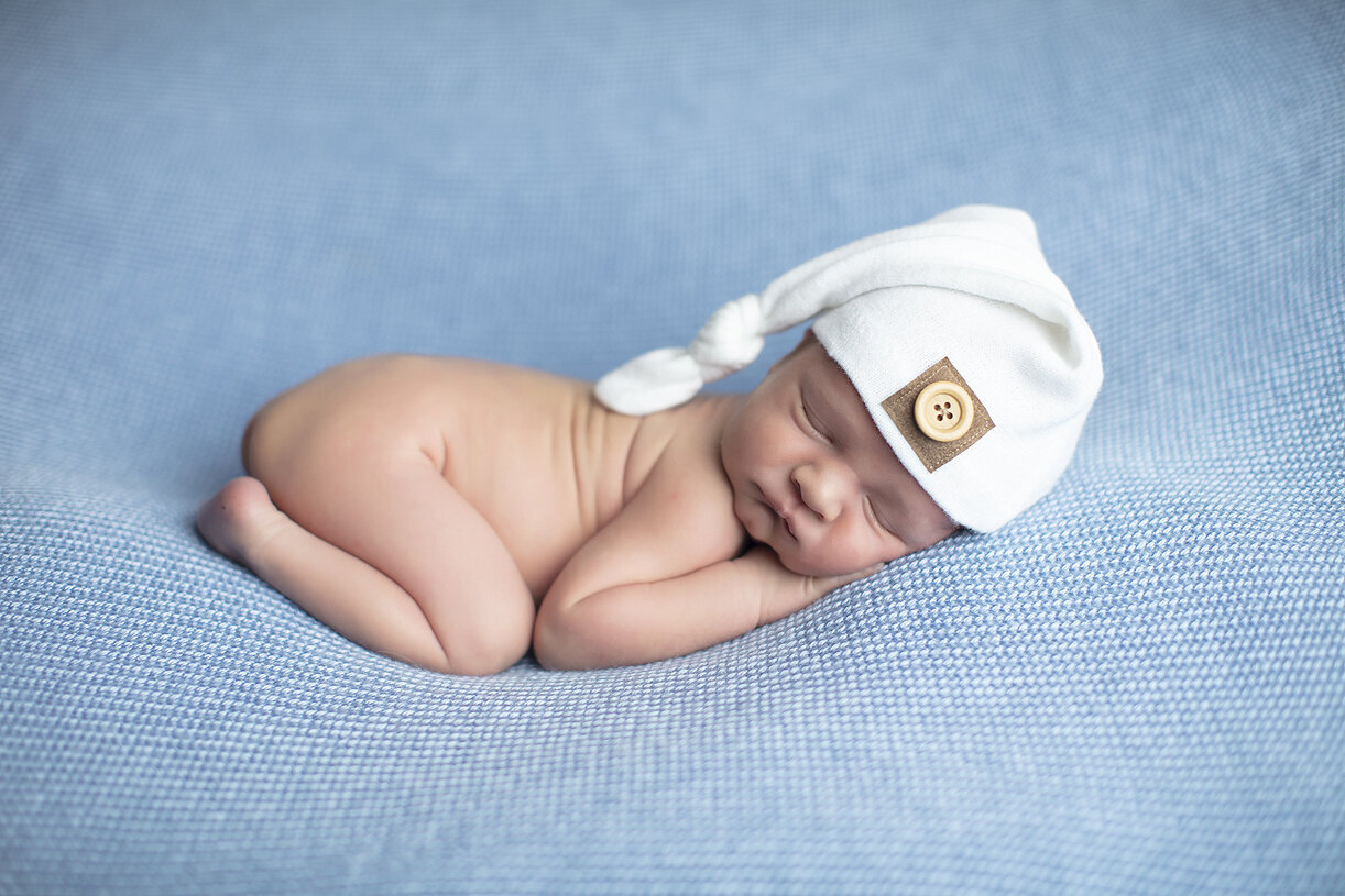 Newborn wearing white hat on blue fabric.
